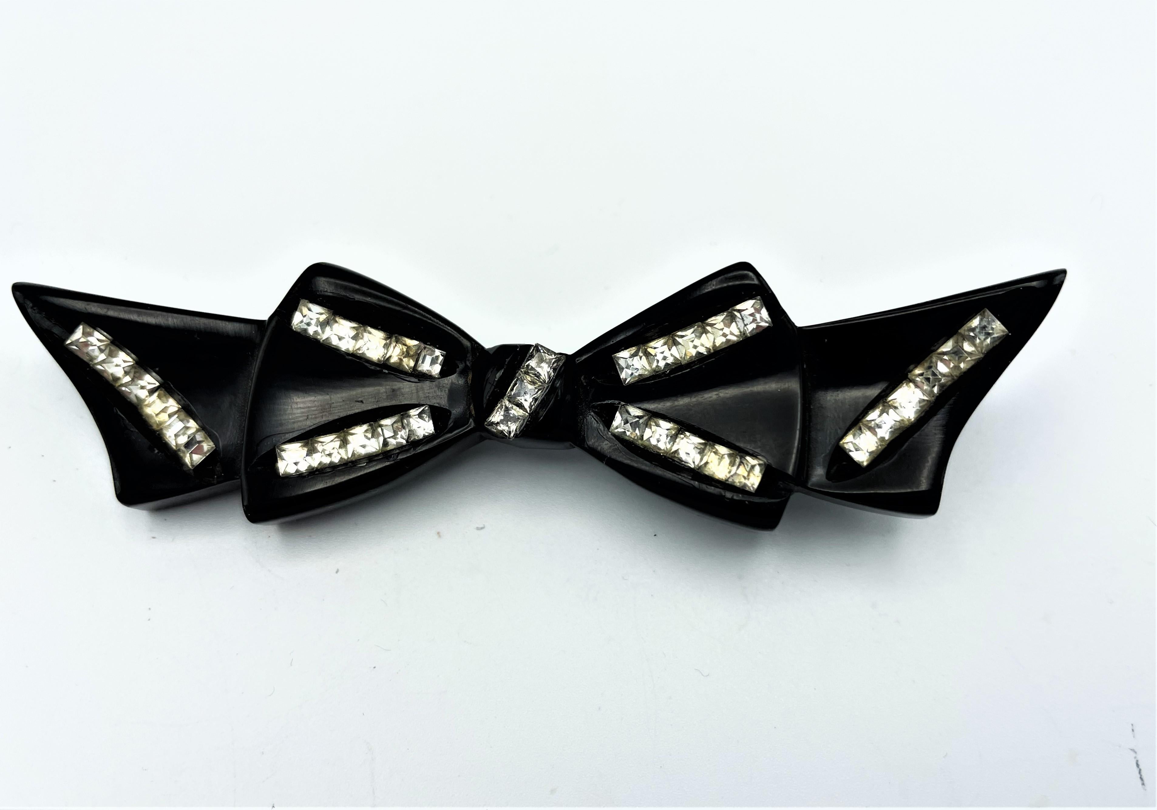 A black Bakelite bow brooch, decorated with many square cut rhinestones embedded in the material.
The deco necklace is sold separately!
Measurement: Width 9,5 cm, Height 2,5 and Deep 0,6 cm. Perfect condition, no missing stones.
