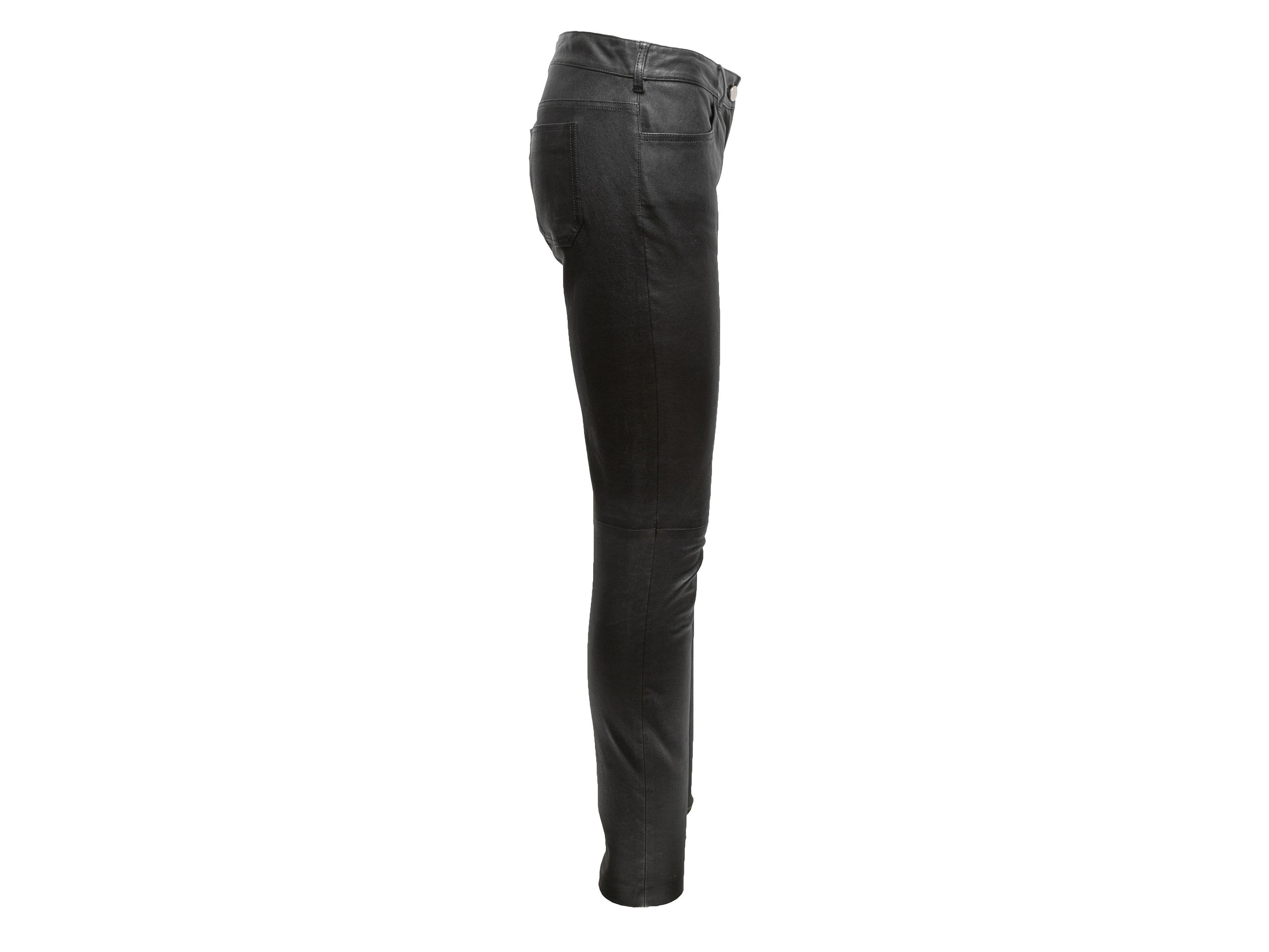 Black leather skinny-leg pants by Balenciaga. Four pockets. Zip and button closures at front. 32
