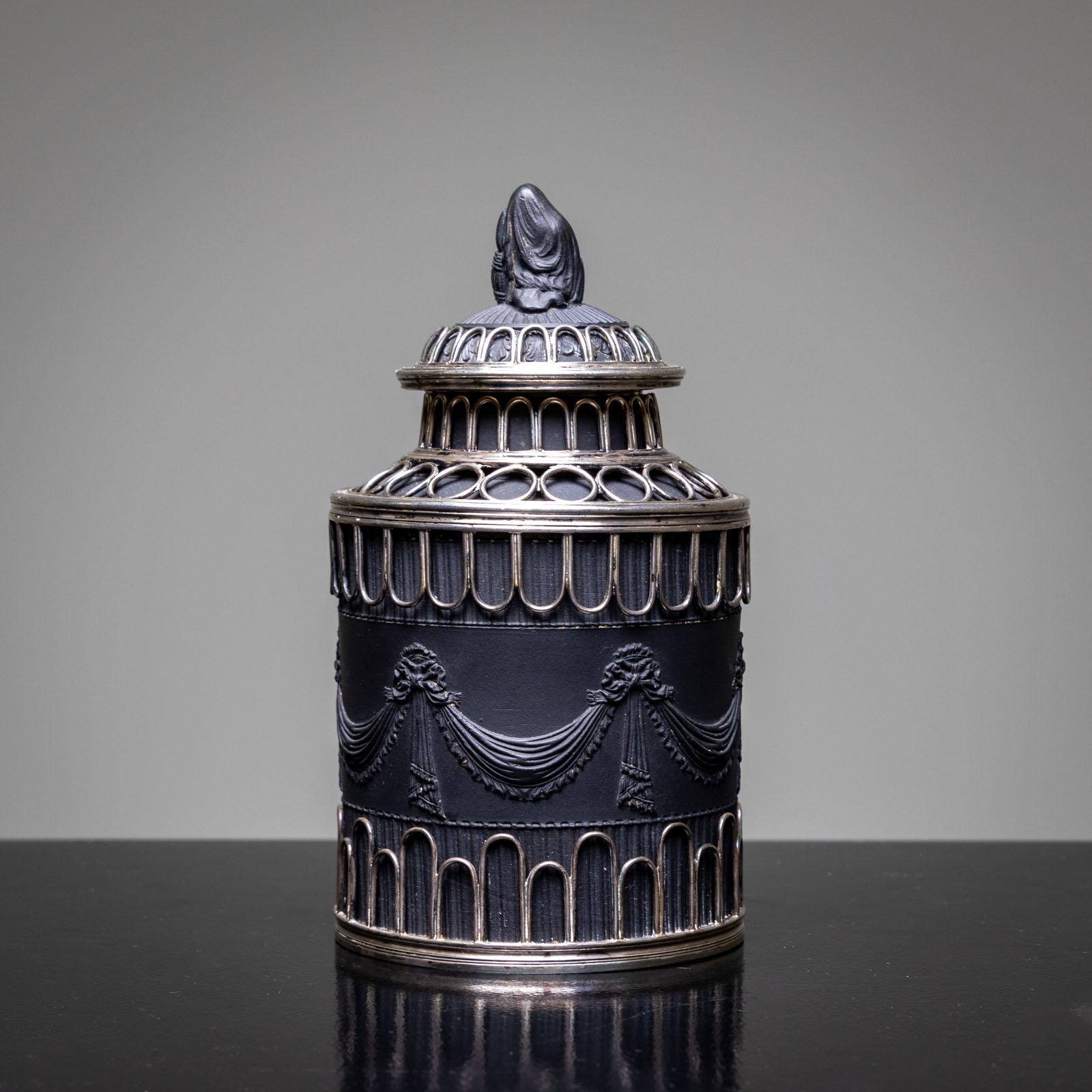 Cylindrical tea caddy made of black basalt with silver mounting and figural nodus.
