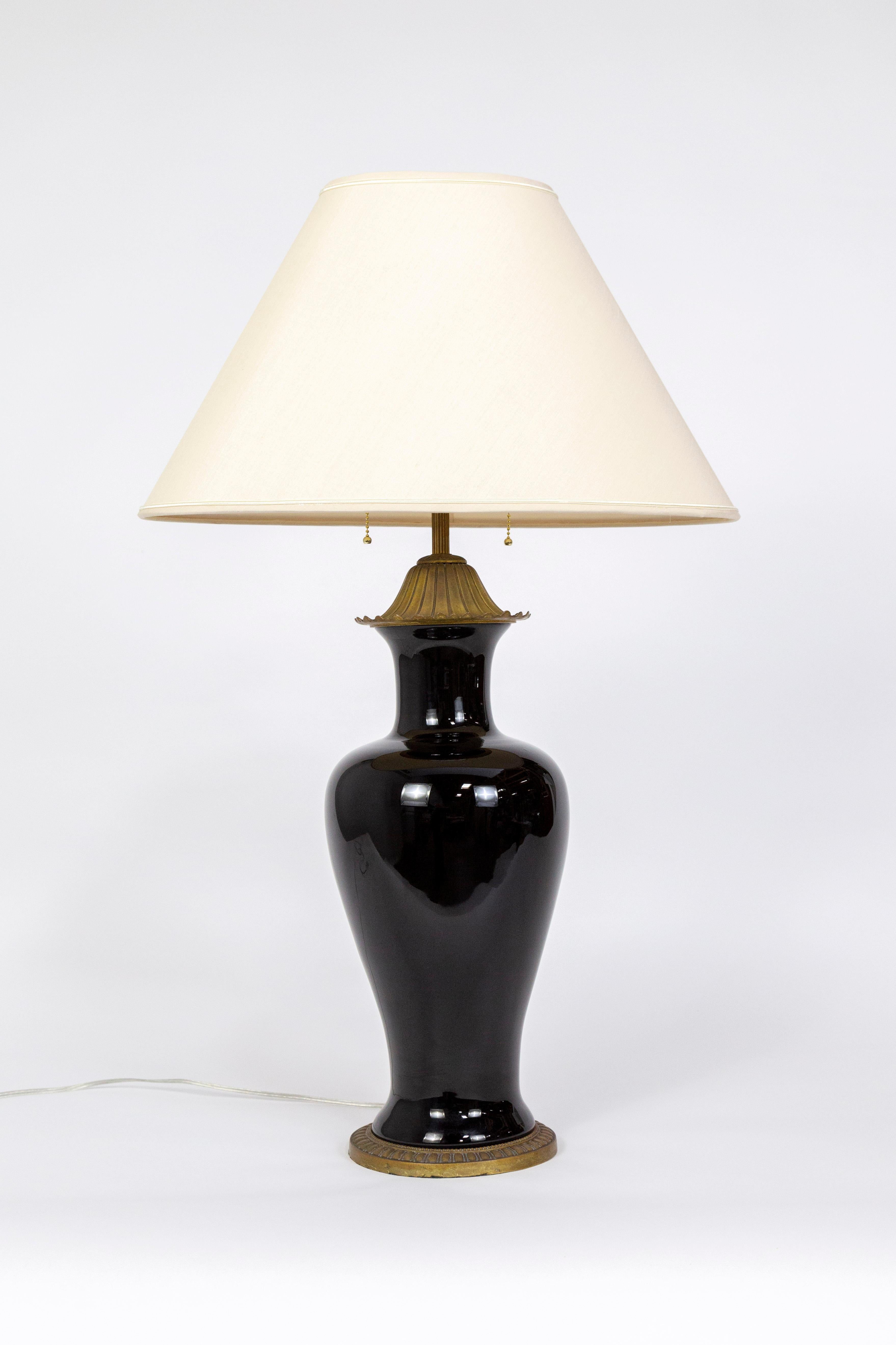 A classical, amphora jar shaped, porcelain lamp glazed in slick black; with a beautifully aged and finely cast brass base, bellflower cap, and ribbed stem. It was made in the 1950s by Marbro Lamp Co. of Los Angeles. Newly wired with two swiveling