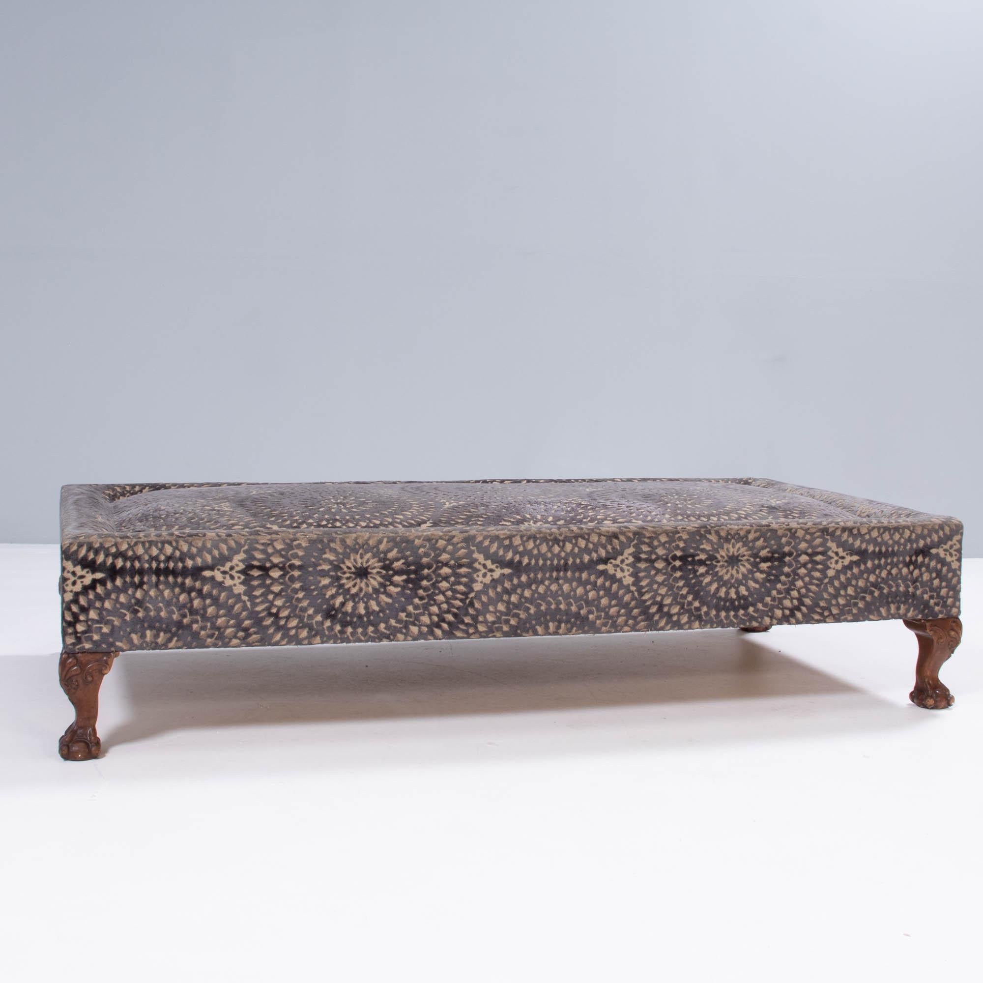 A beautifully made ottoman, fully upholstered in black and beige jacquard velvet, featuring an intricate circle pattern.

The large rectangular ottoman sits on ornately carved wooden legs and features a sloped edge detail.

The generous size