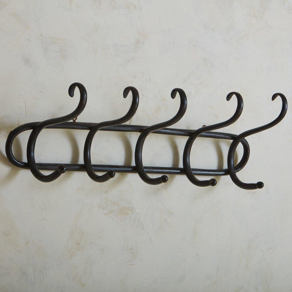 A French wall mounted coat rack constructed with bentwood and painted black. This rack features five dramatically curved arms, which attach to a cylindrical backplate. This elegant fixture would look beautiful in an entryway or mudroom. Sourced in