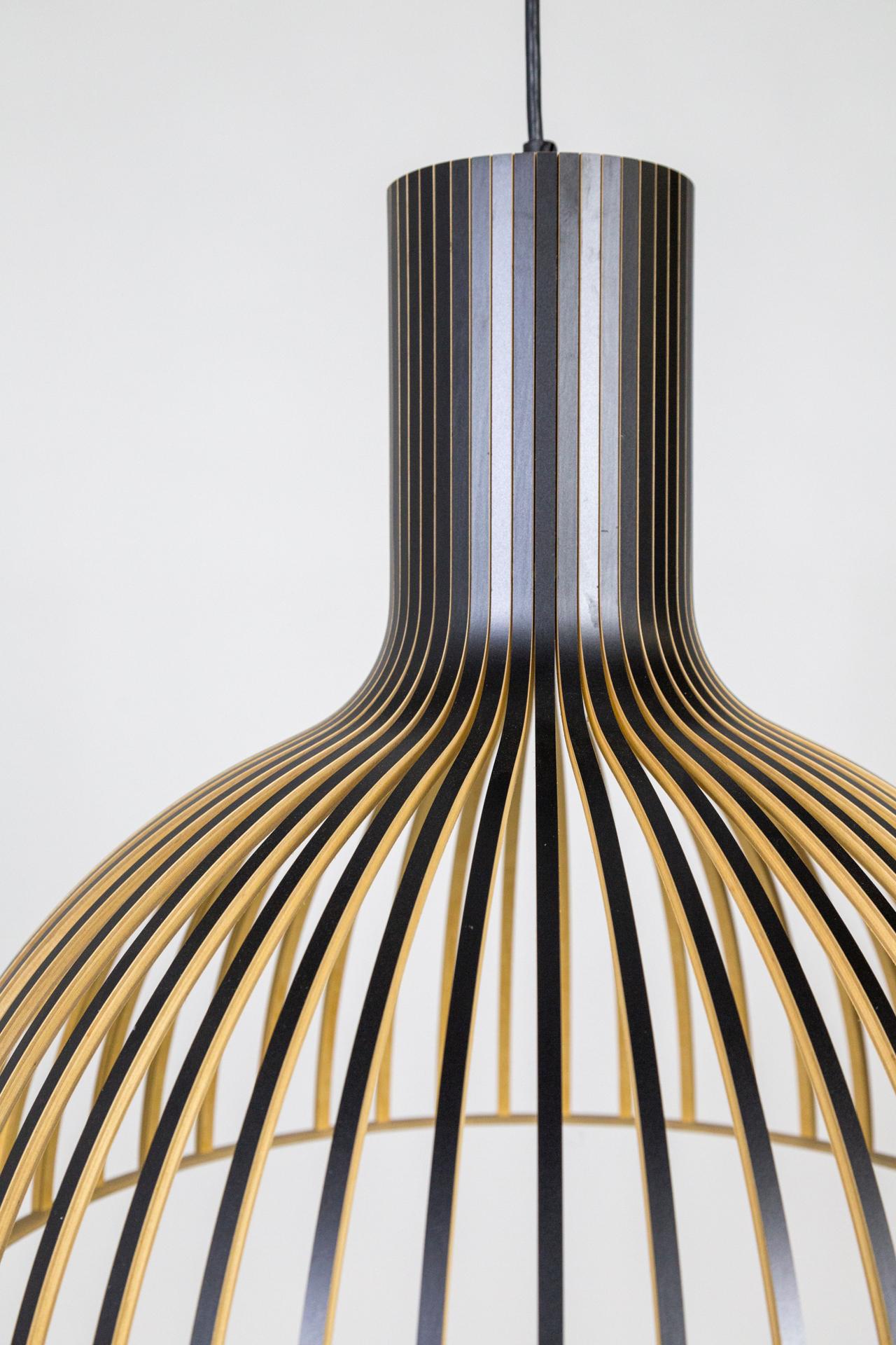 This pendant light features a shade made from black laminated birch slats connected to a plywood ring; suspended with a black cord and canopy. Finland-based Secto Design specializes in modern designer lamps with handmade shades crafted from the