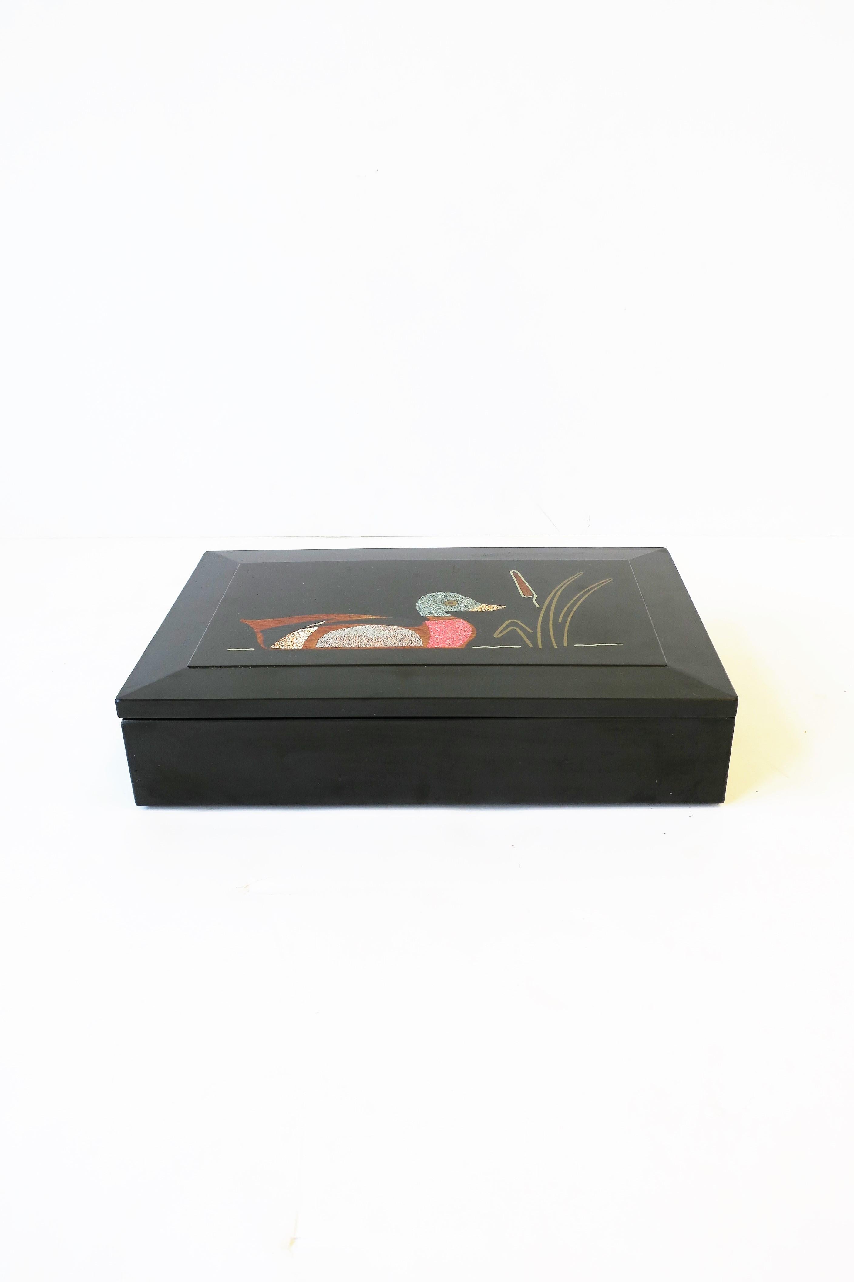 A black resin rectangular box with mosaic inlaid mallard duck bird on pond with cattail plant flower; all inlaying was done by hand with natural materials outlined in brass, circa 1970s, USA. Maker's mark on back. Great as decorative box or to hold