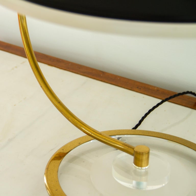 A Bauer designed Lucite and brass desk lamp with a black shade rimmed with frosted Lucite. The base is made of a circular stepped brass, clear Lucite and frosted Lucite, with the brass arm supporting the shade. 

The Bauer Lamp Company operated