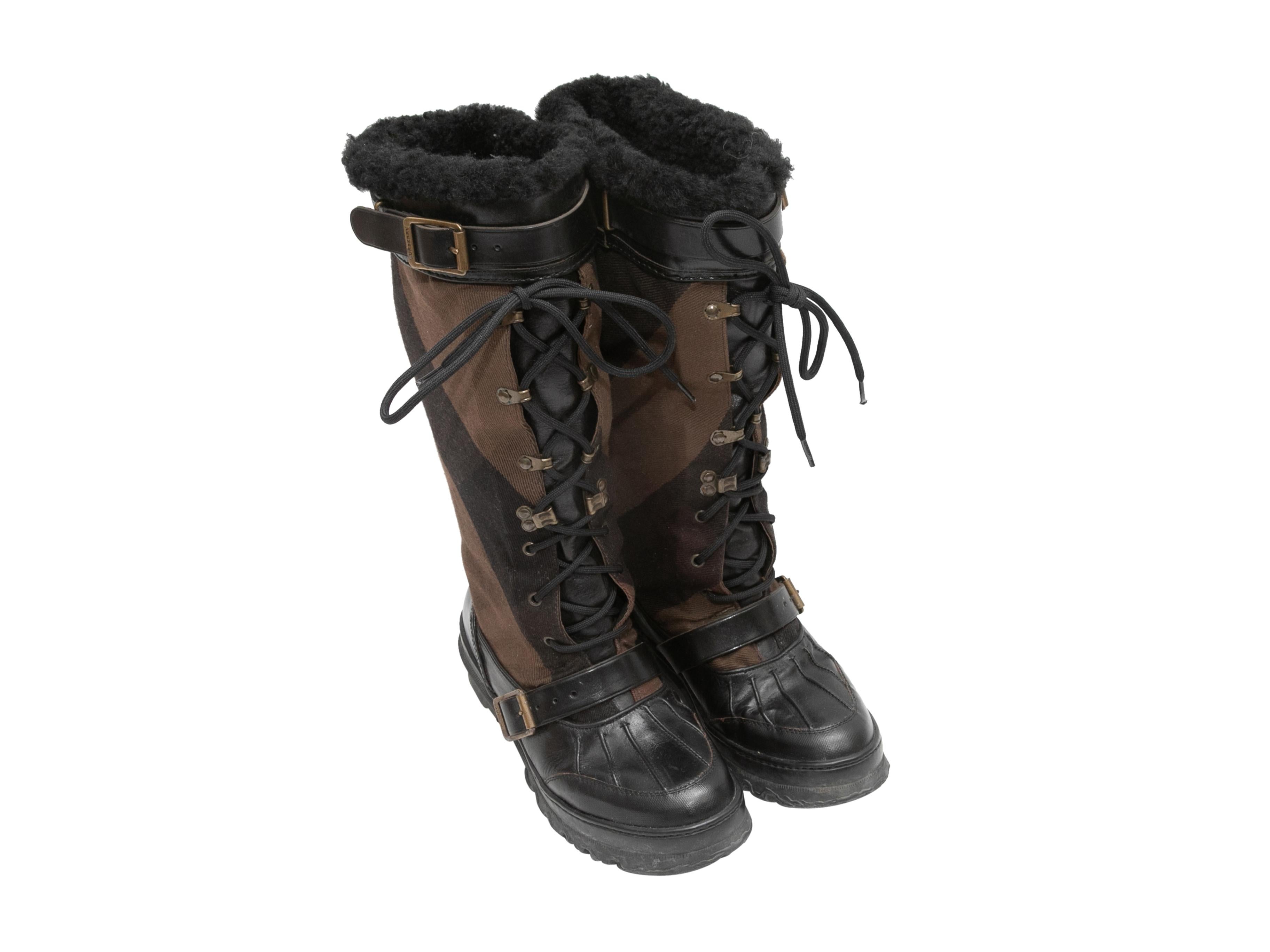 Black and brown shearling-lined Nova Check duck boots by Burberry. Buckle accents. Lace-up tie closures at tops. 13.5