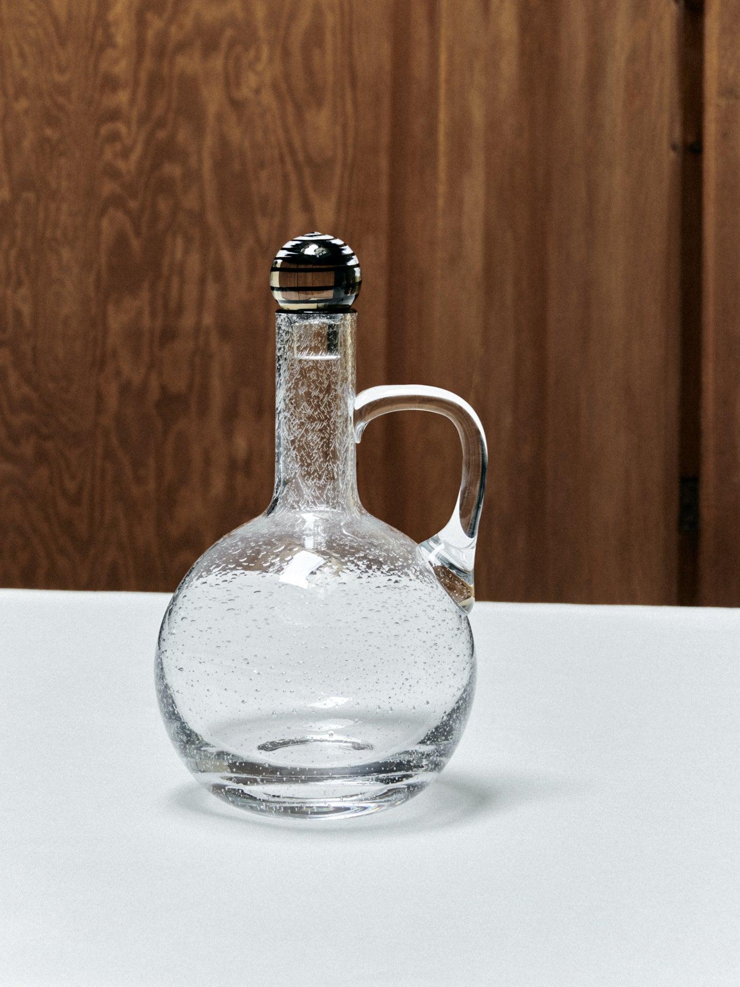 Caraffa in vetro con tappo nero, collezione S.R. di Louise Roe.
Accentuata da un elegante bordo nero, la collezione Bubble Glass di Sophia Roe reinterpreta in modo sottile la serie originale di Louise Roe. Celebra l'arte della soffiatura del vetro,