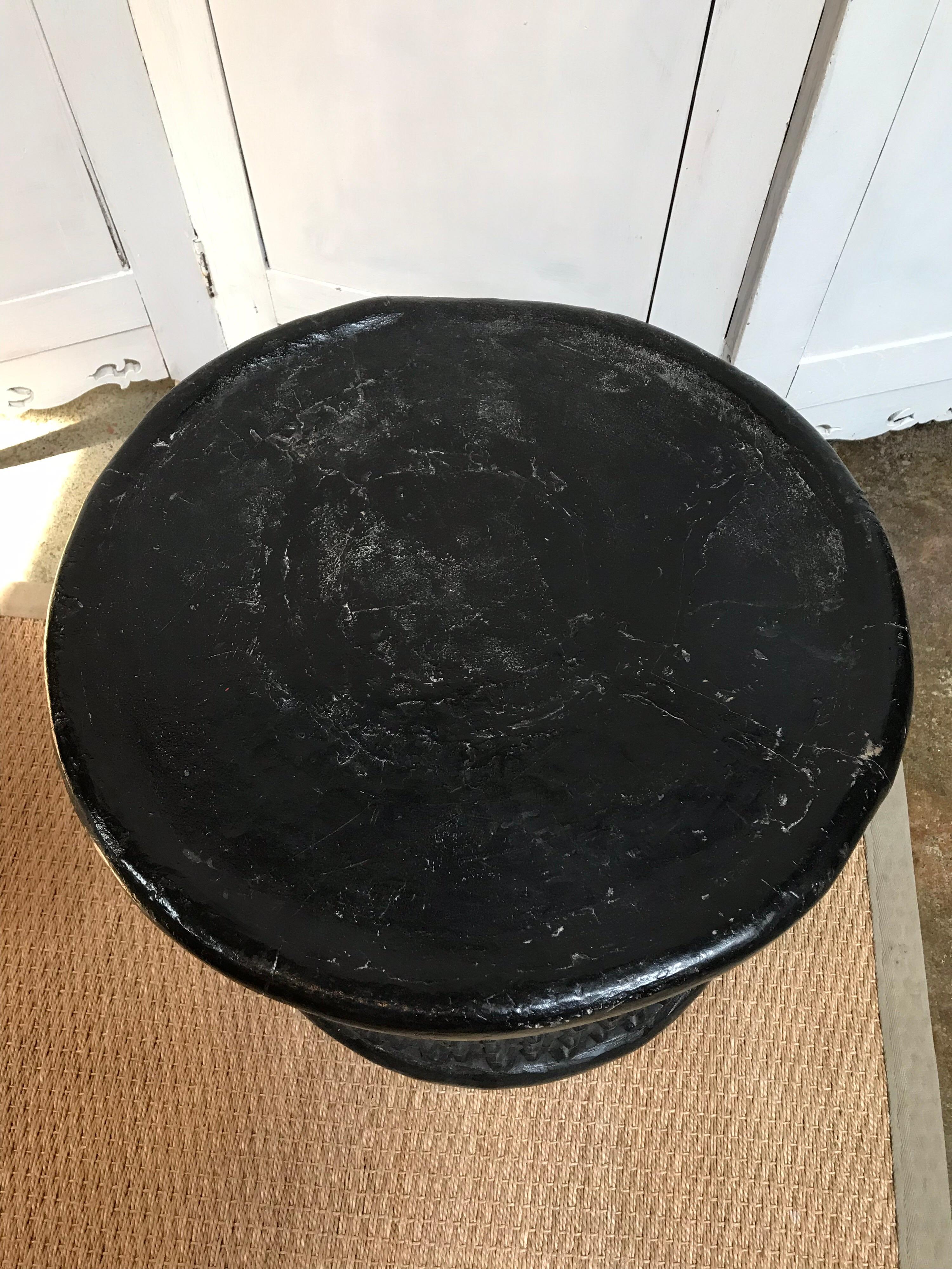 This circular table was handmade by the Cameroon people from Central Africa. It's black with a smooth top and has a bumpy textured, grated pattern for its base.