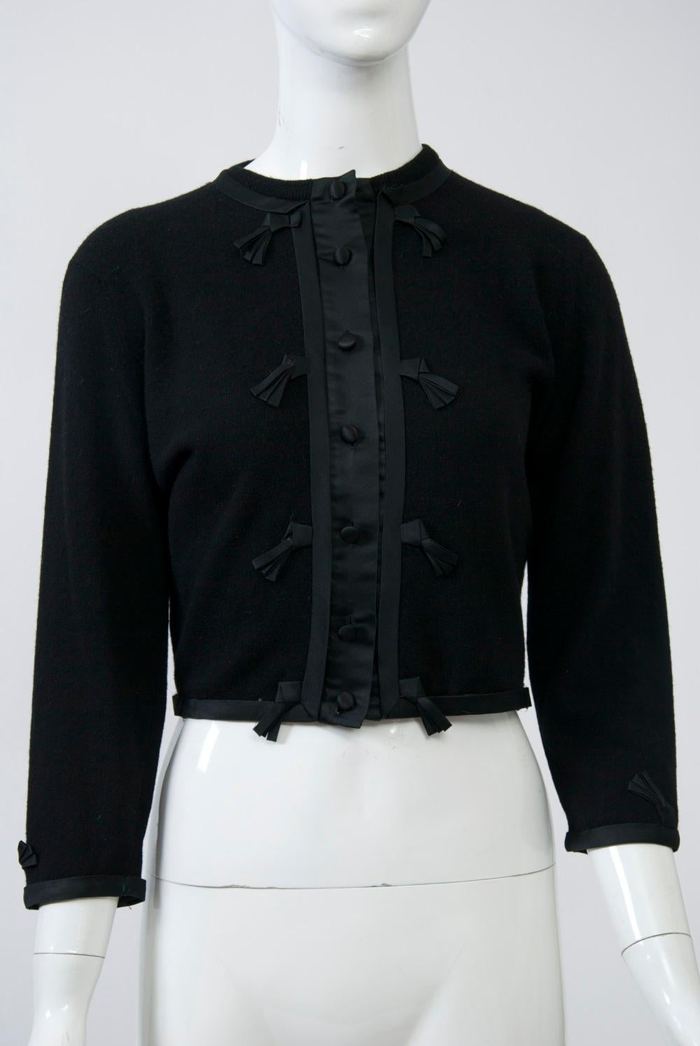 Cropped vintage cardigan in black cashmere featuring black satin trim further adorned with small fringe detail. Matching satin buttons. Unlined. A lovely example of the embellished cardigans popular during the 1950s and ‘60s. Petite/small size.