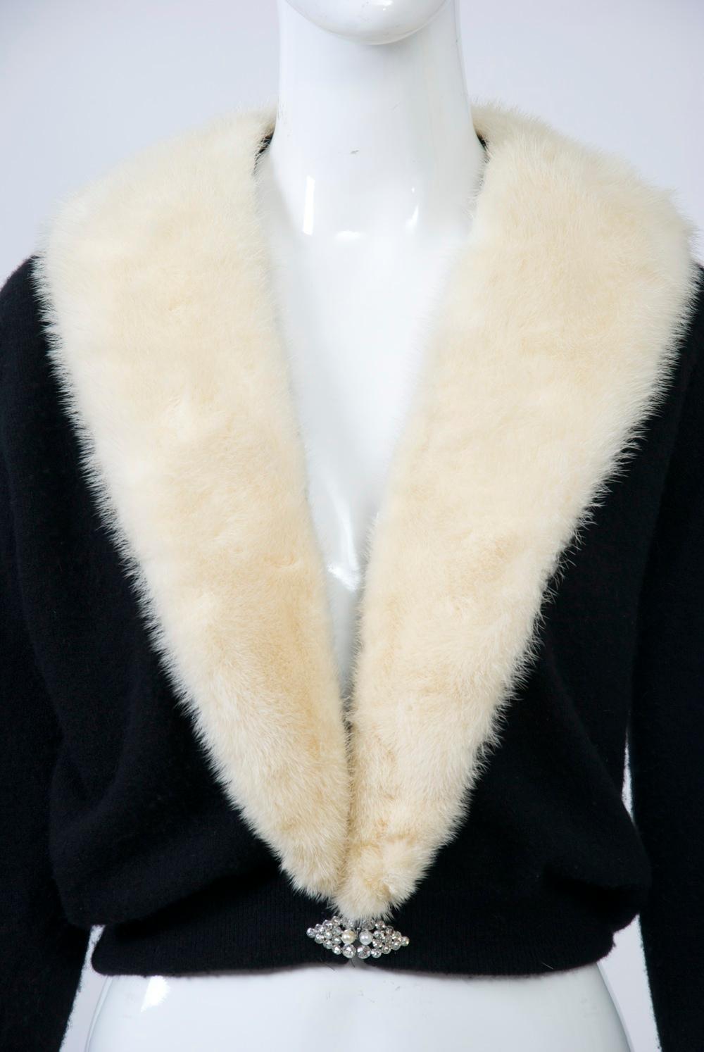 1950s-'60s black cashmere cardigan with white mink shawl collar, pearl accents on the turned-back cuffs, and a rhinestone and pearl clasp at the waist. The collar is attached via a tape with snaps so the sweater can be cleaned. Unlined.
Approximate