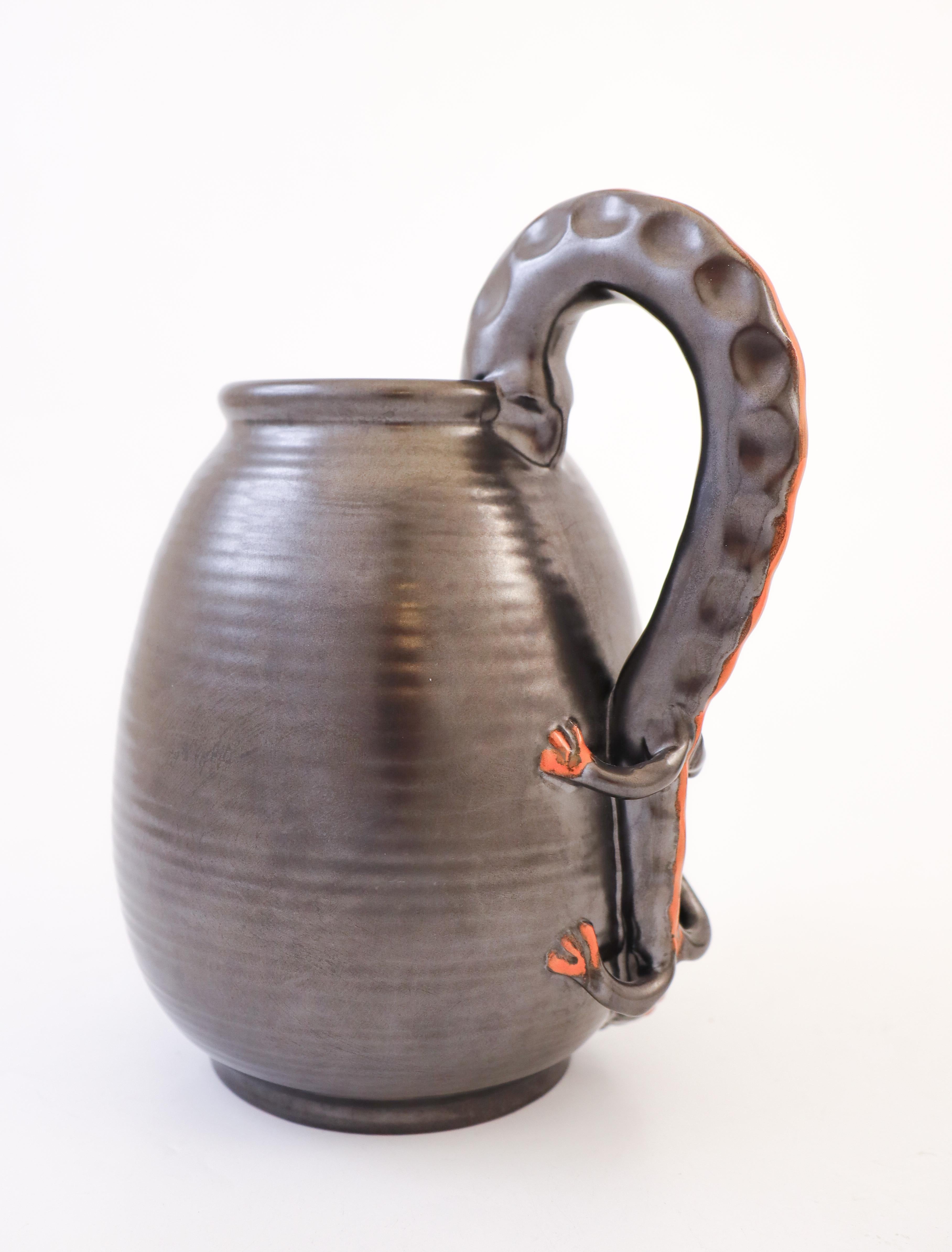 Un superbe pichet Art déco en céramique noire conçu par Upsala Ekeby dans les années 1930.  Il est doté d'une superbe poignée en forme de lézard grimpant dans le pichet. Il mesure 22 cm de haut et est en excellent état.
