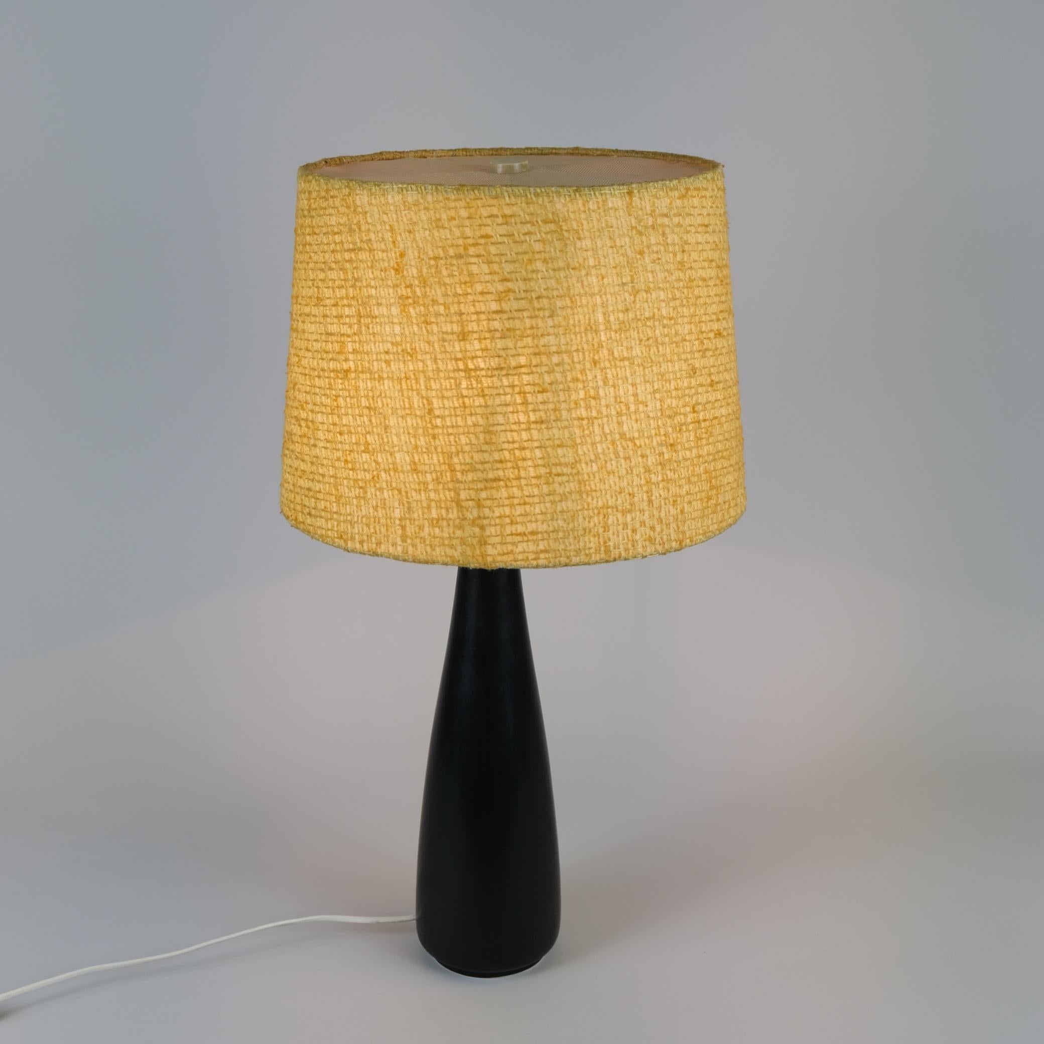 Una bella lampada da tavolo vintage in ceramica nera, ottone e paralume originale giallo. La lampada è piuttosto alta per essere una lampada da tavolo, con un'altezza di 47 cm senza paralume (68 cm con). La lampada è molto probabilmente prodotta da