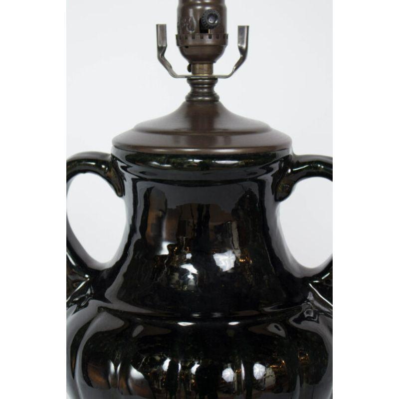 Black ceramic table lamp in an urn form. glossy black glaze. A narrow neck with two curved arms. widens in the center in a pumpkin shape. Dark patinated metal vase cap and black carved wooden base. Single socket and harp. Rewired with new hardware,