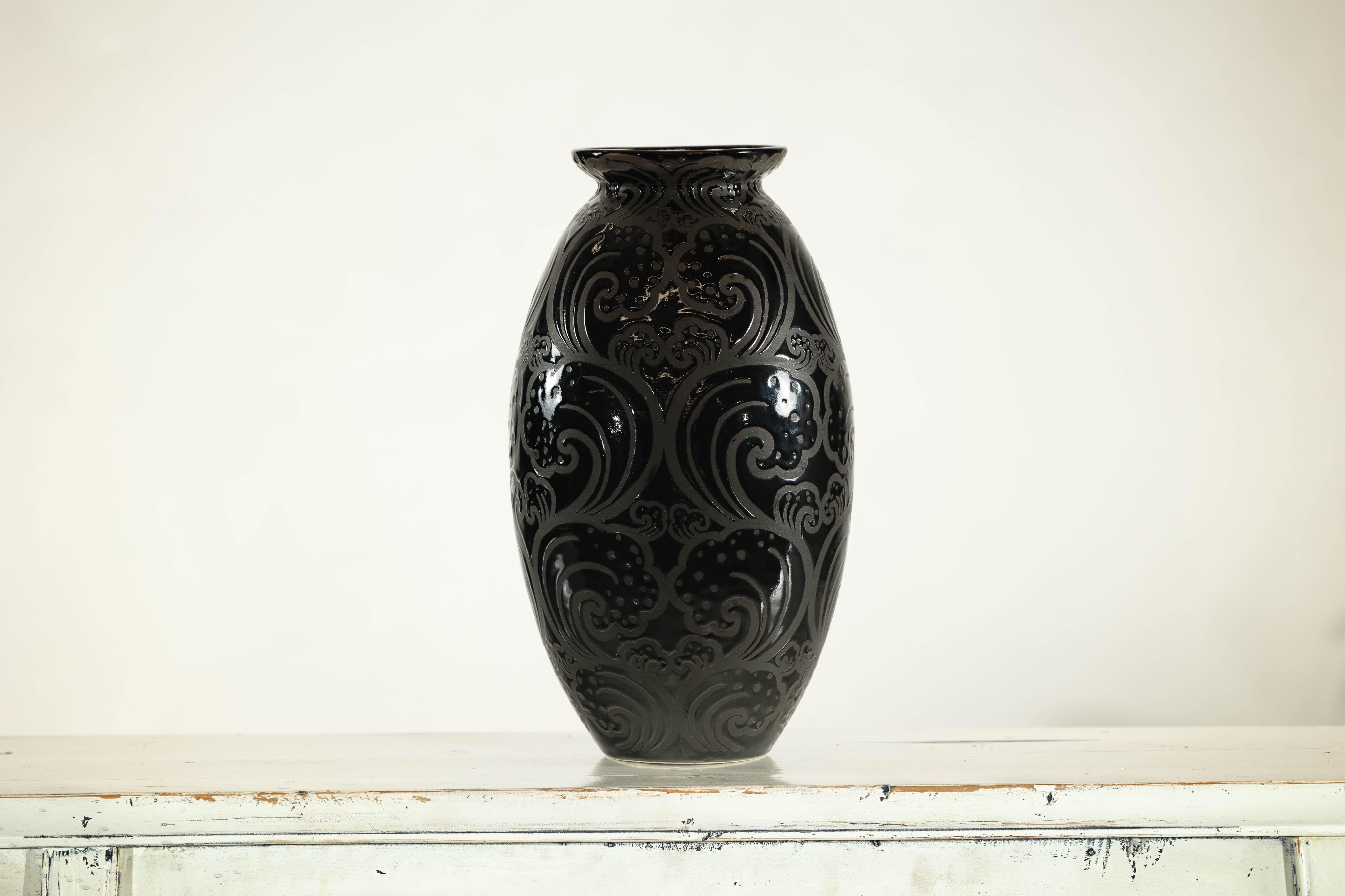 With its high-gloss finish and richly textured surface, this vintage ceramic vase commands attention through its sculptural depth and modern palette. The vessel is entirely coated in black glaze, but the sinuous raised swirl pattern catches the