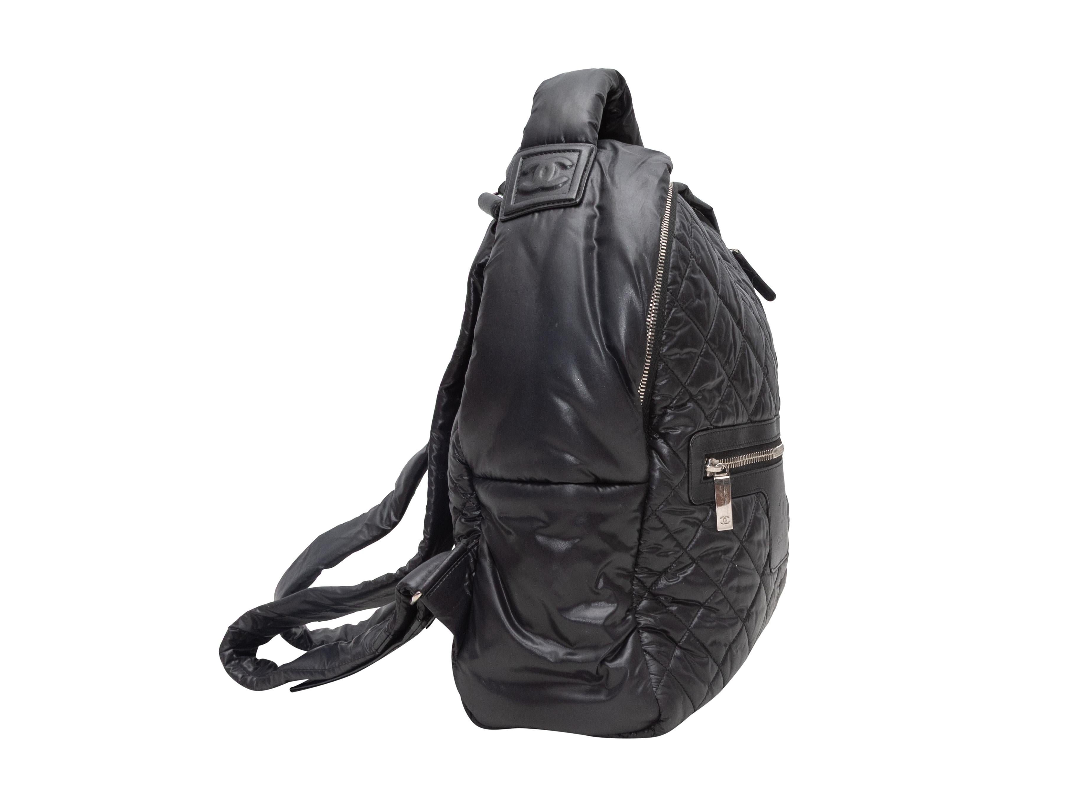 Mochila acolchada Coco Chanel negra. La mochila Coco Cocoon tiene un cuerpo de nailon acolchado, herrajes plateados, adornos de piel, un bolsillo frontal con cremallera, un asa plana superior, dos correas ajustables para el hombro y un cierre