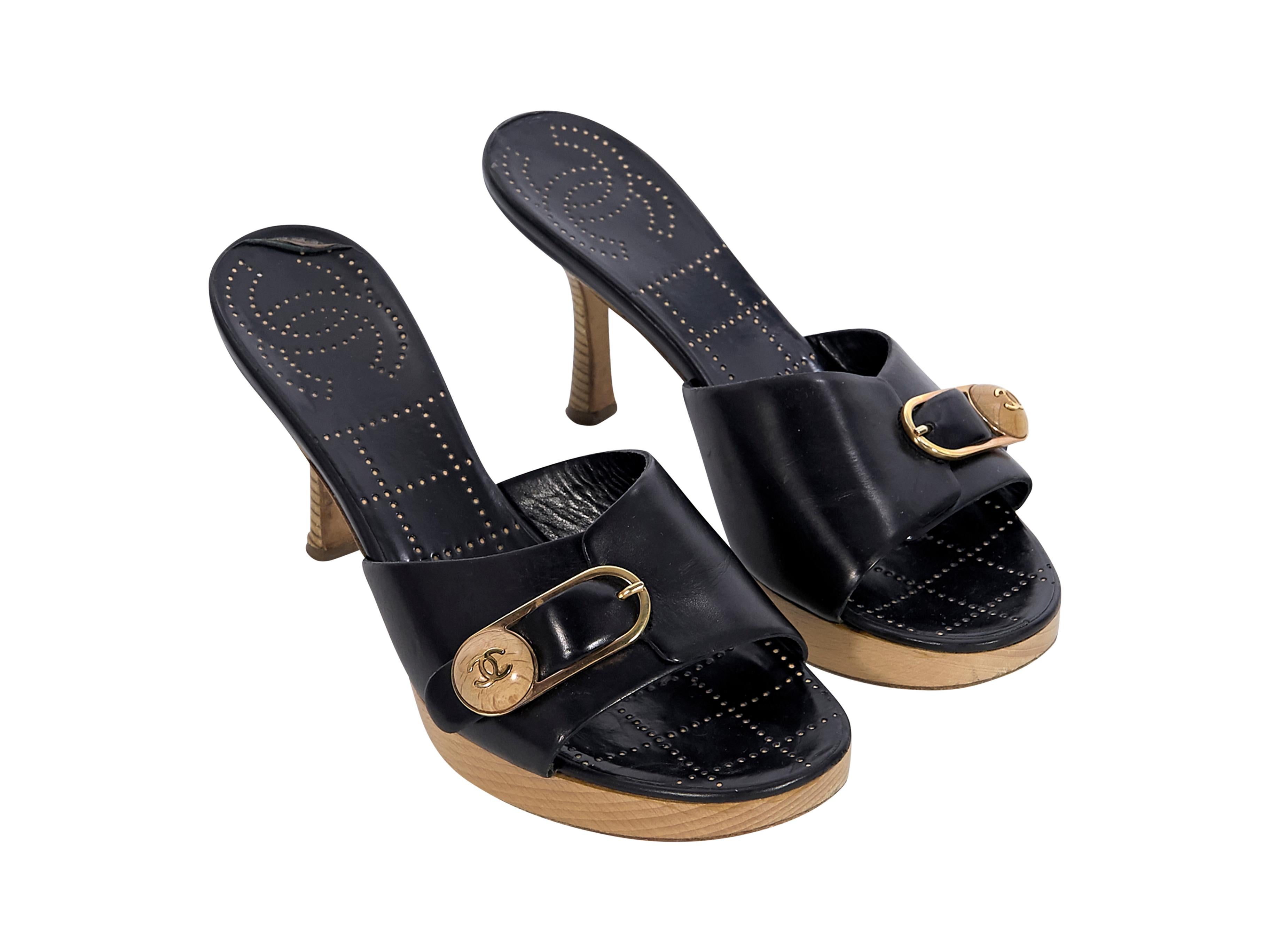Product details:  Black leather heeled mules by Chanel.  Gold-tone logo buckle at vamp. Round toe. Wooden heel and platform. Slip-on style. Label size FR 37. Style with leather mini shorts. 3
