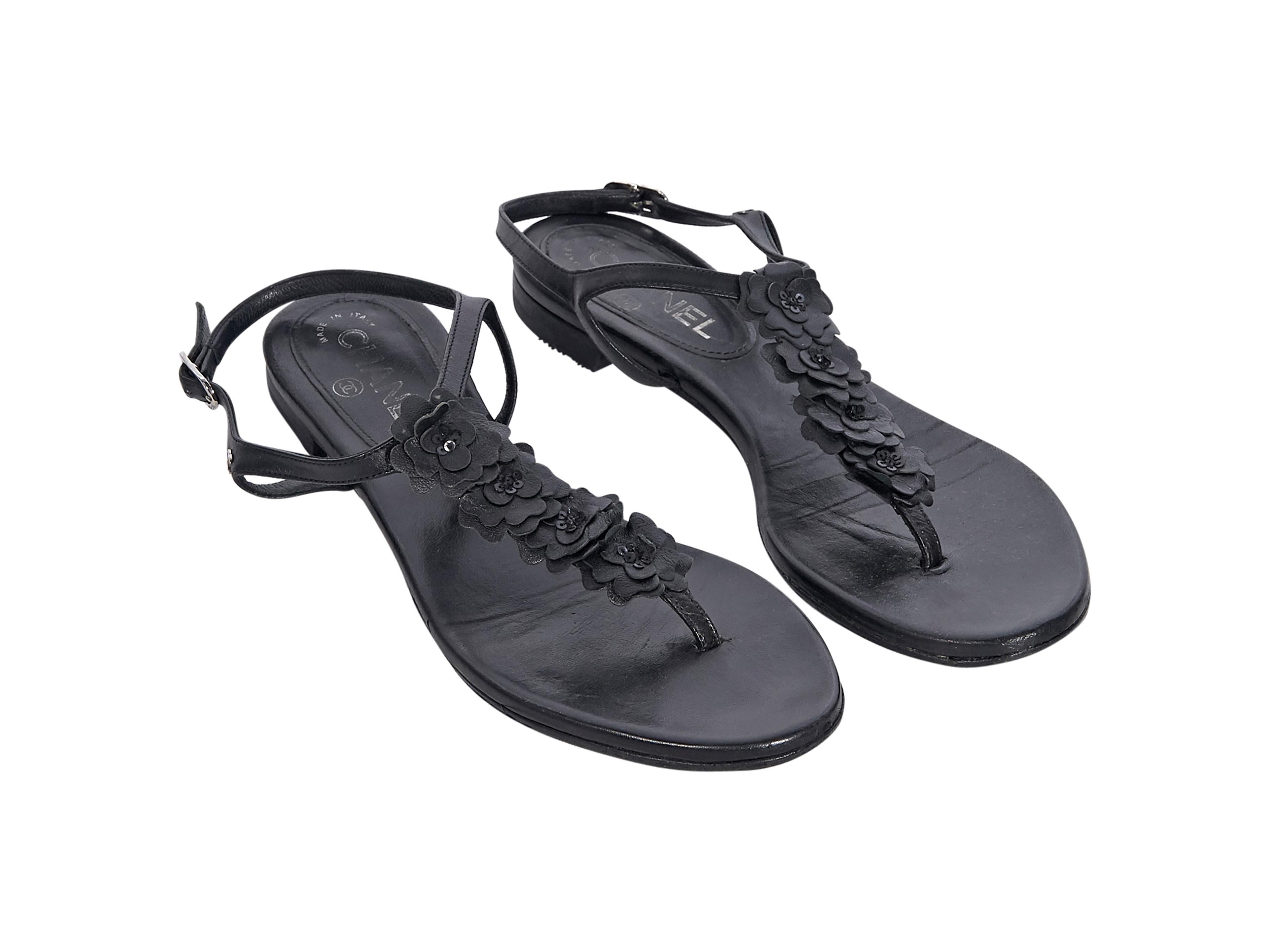Product details:  Black leather thong sandals by Chanel.  Adjustable ankle strap.  T-strap accented with camellia floral applique.  Silvertone hardware.  
Condition: Pre-owned. Very good.
Est. Retail $ 995.00