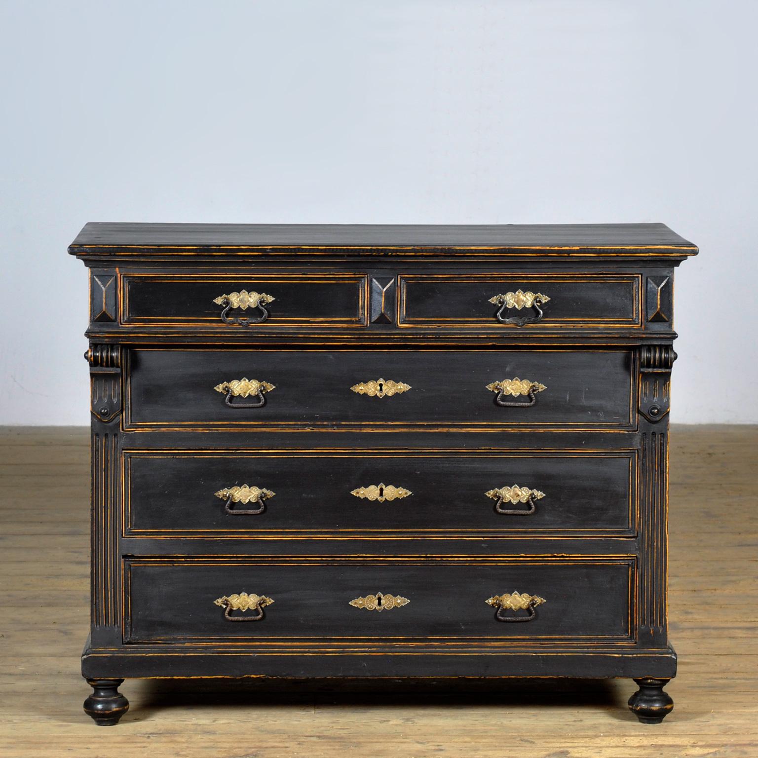 This late 19th-century chest of drawers is made of pine and oak with neoclassical influences. The black finish has a distressed look, with the underlying wood visible in some areas. The chest has two smaller top drawers above three full-width