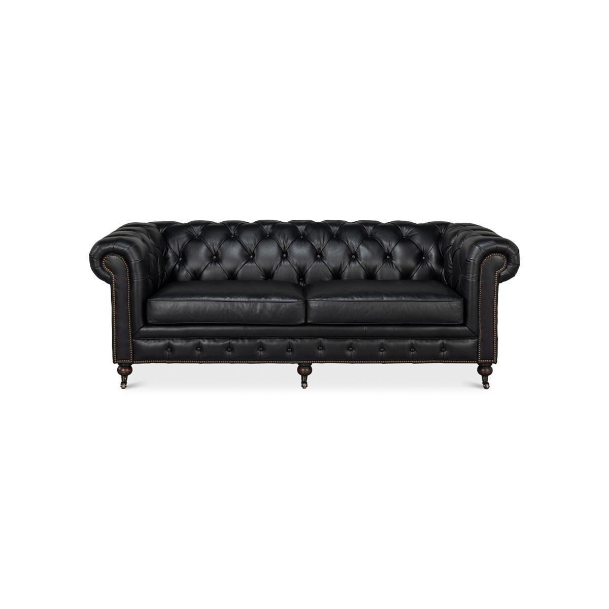 A vintage style classic English Chesterfield leather upholstered sofa, with top-grain leather. With a tufted backrest and rollover arms, and two padded cushions raised on turned mahogany feet with brass casters and finished with brass nailhead