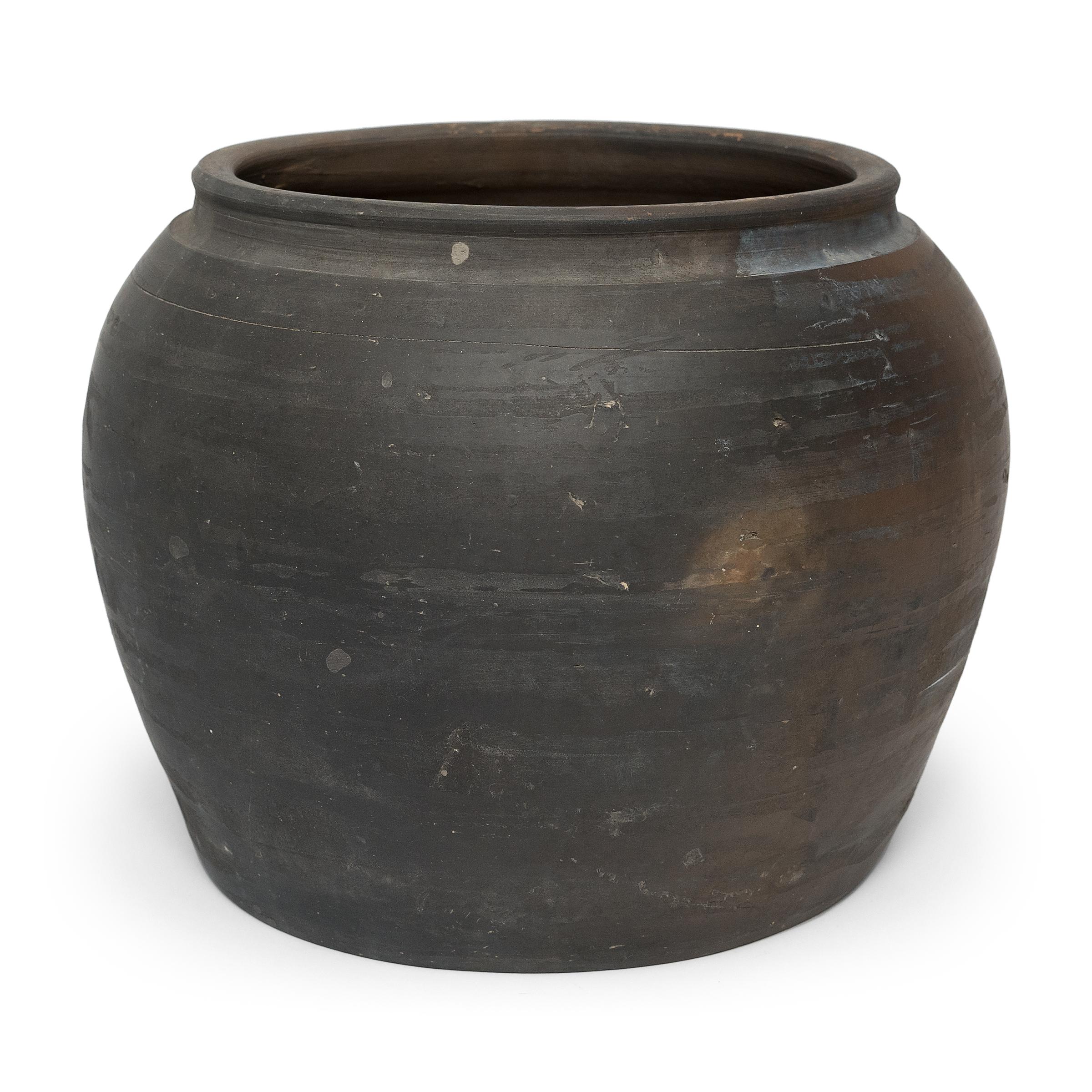 Sculpted by artisans in China's Shanxi province, this vessel has a smoky black exterior on one side that transitions into a golden brown on the other. The squat clay vessel has a quiet simplicity, shaped with balanced proportions and an undecorated,