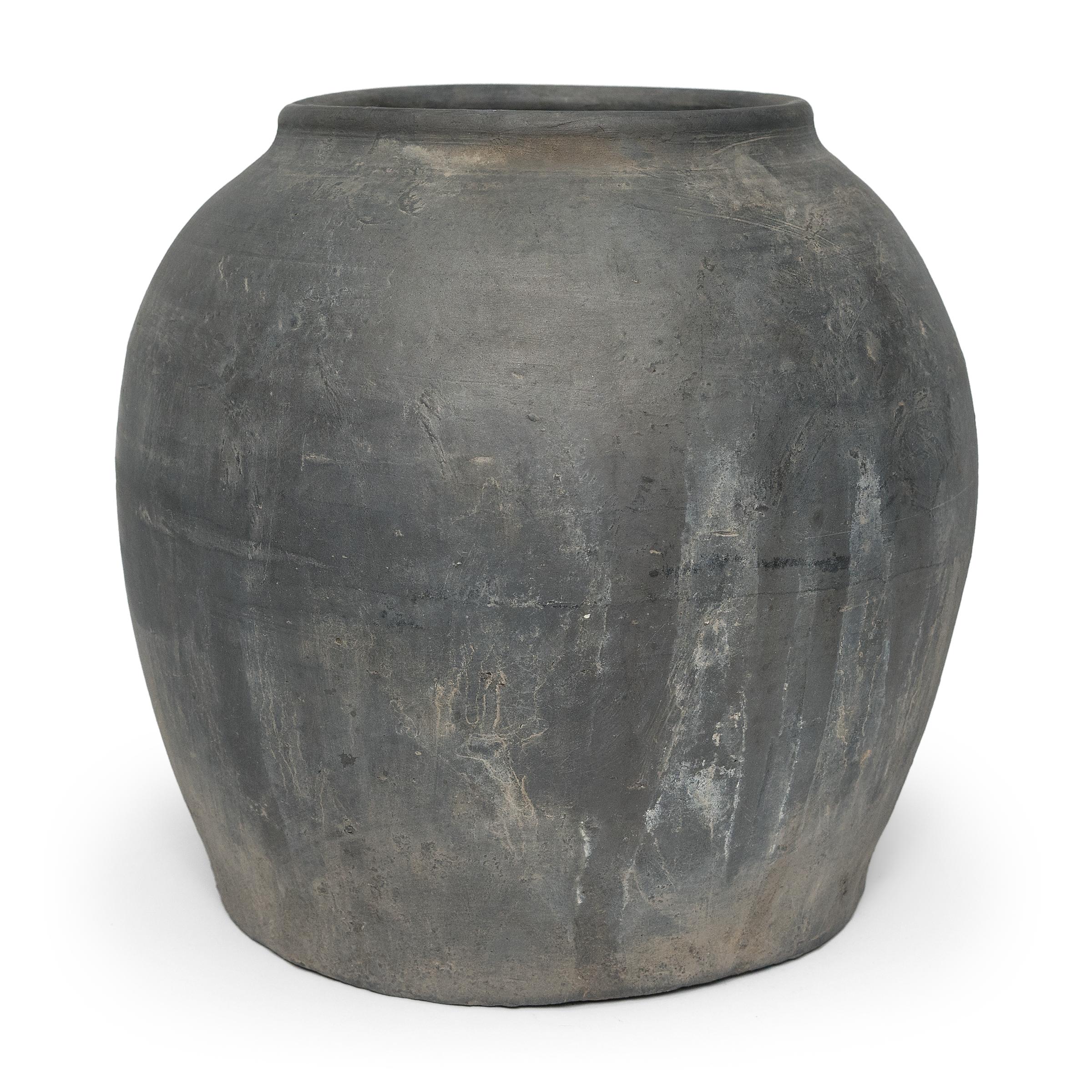 Sculpted during the early 20th century in China's Shanxi province, this vessel has a smokey grey exterior with balanced proportions and a beautifully irregular unglazed surface. Charged with the humble task of storing dry goods, this earthenware jar