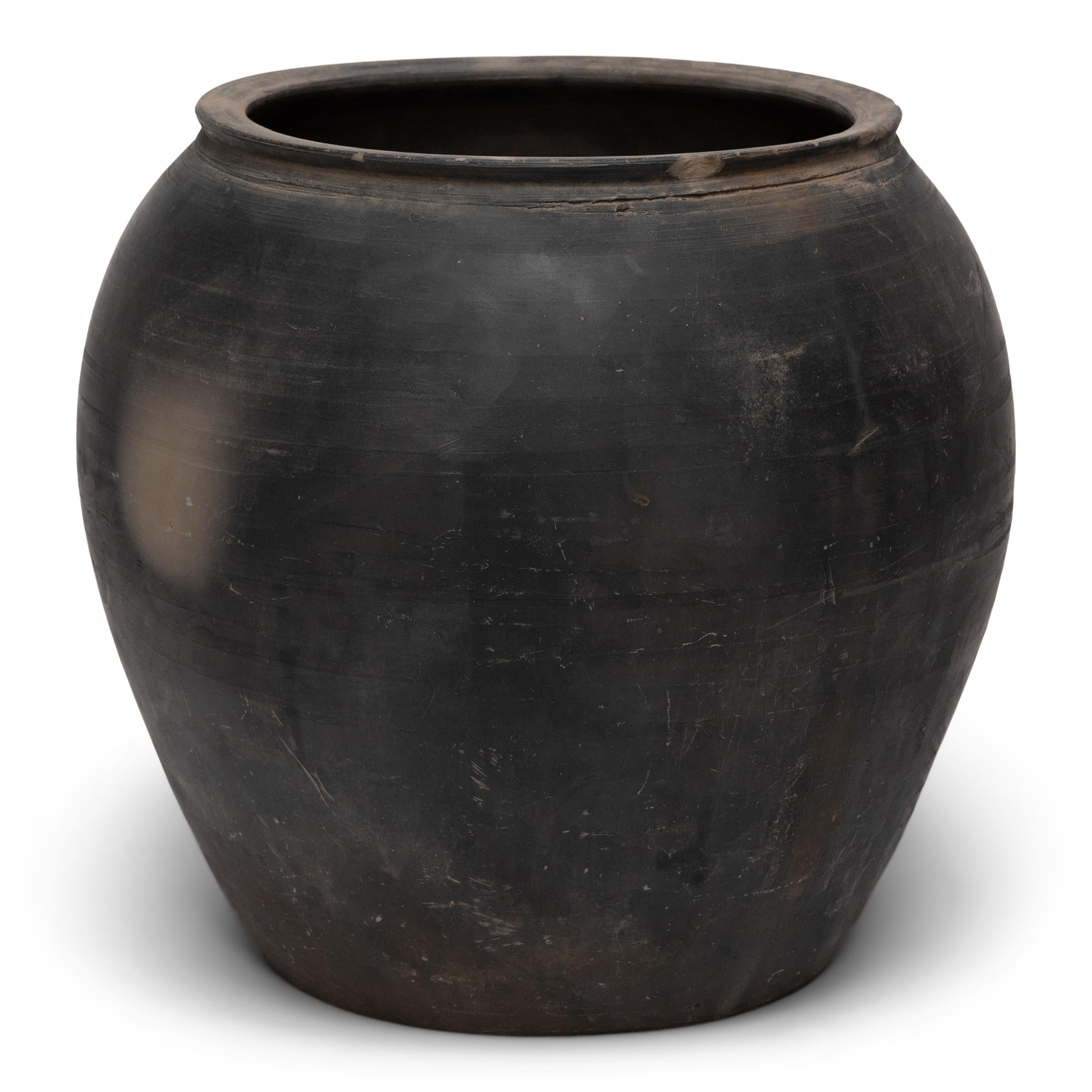 Sculpted during the early 20th century in China's Shanxi province, this terra cotta vessel has a smoky taupe-black exterior with balanced proportions and a beautifully irregular unglazed surface. Charged with the humble task of storing dry goods,