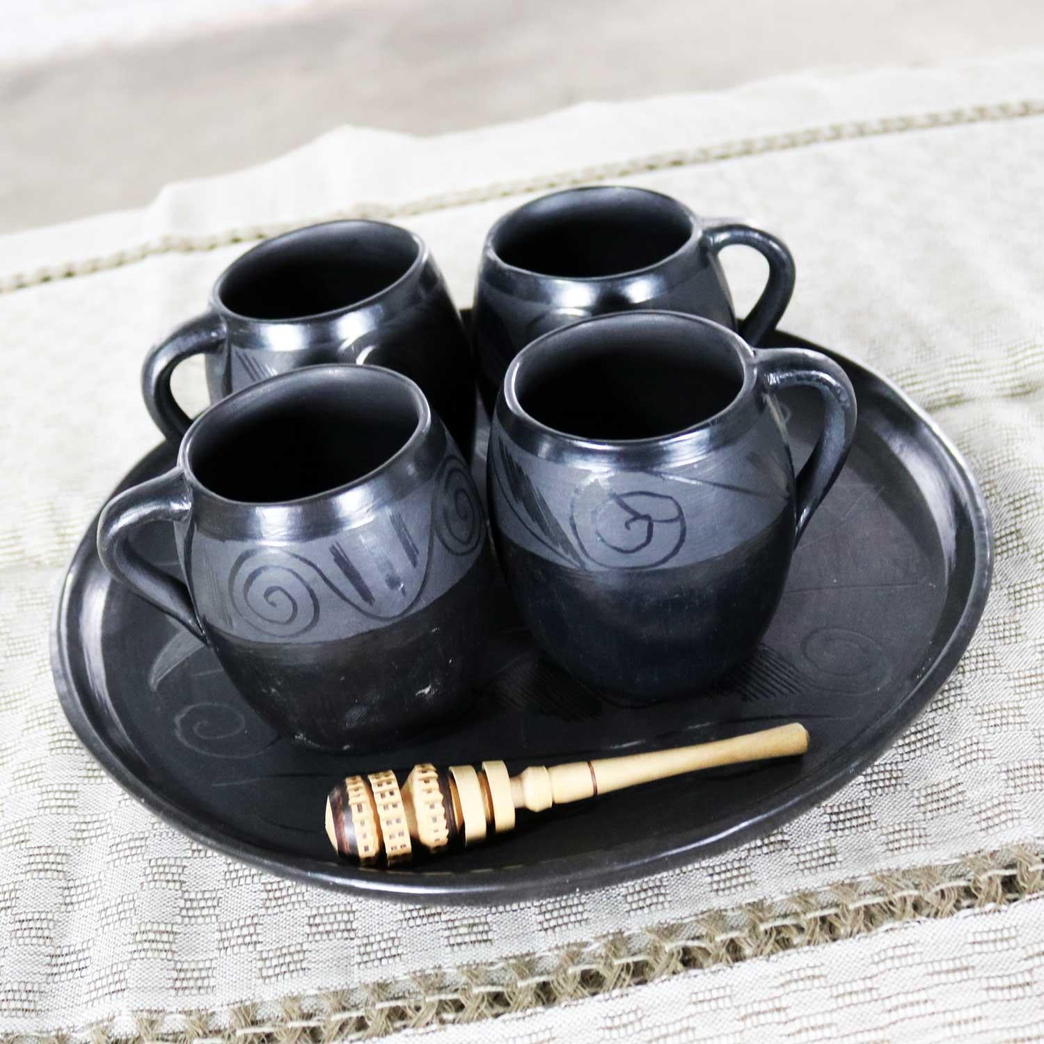 Handsome black clay or barro negro pottery hot chocolate set most likely from Oaxaca, Mexico consisting of 4 mugs, tray with Fish design, and wooden cocoa whisk. All pieces are in wonderful vintage condition with no outstanding flaws that we have