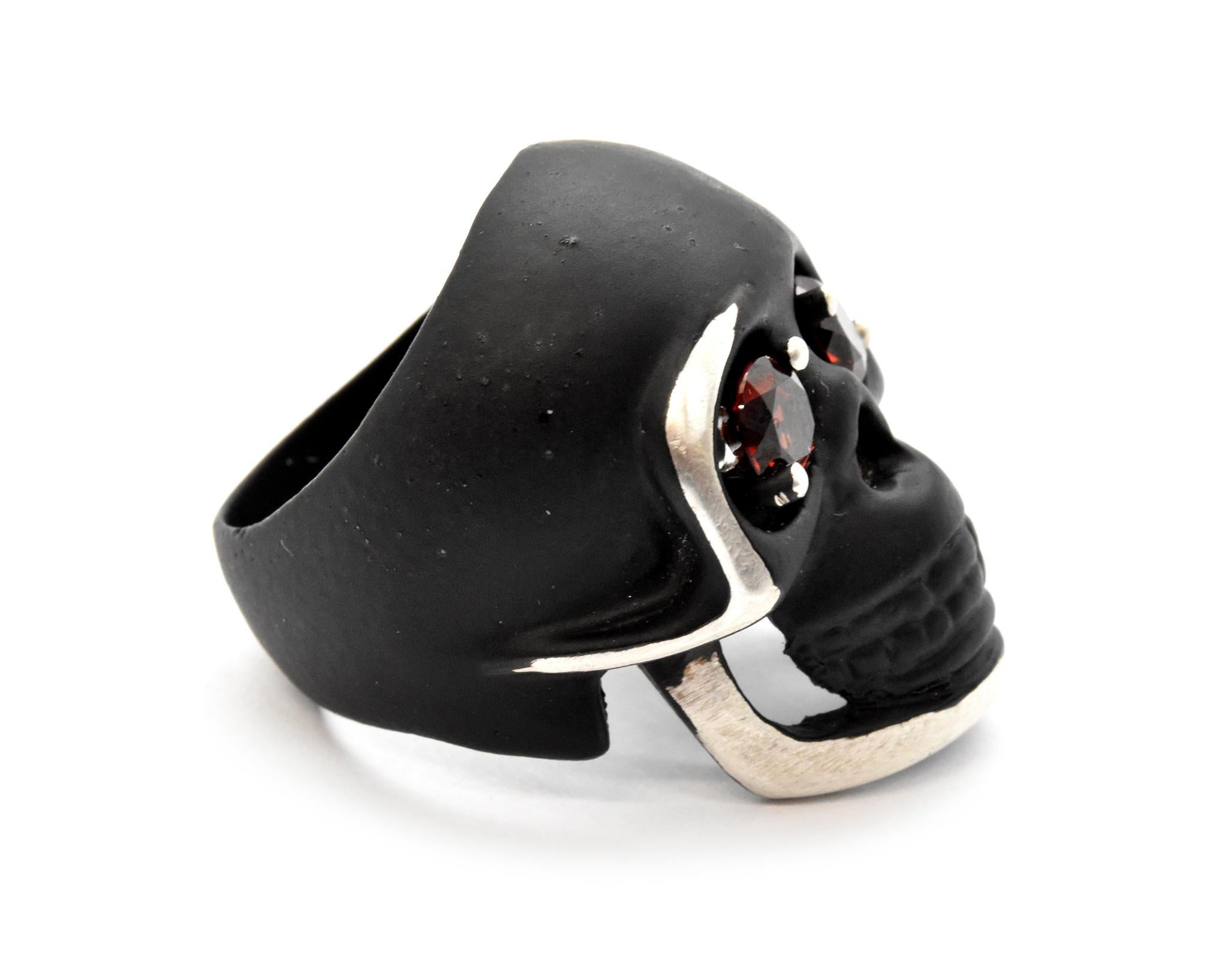 This is a sterling silver skull ring coated in black and set with garnet in each of the eyes. Each garnet is held in place by two prongs, each garnet measures 5.48mm. Ring size is 7 and total weight is 18.45 grams.
