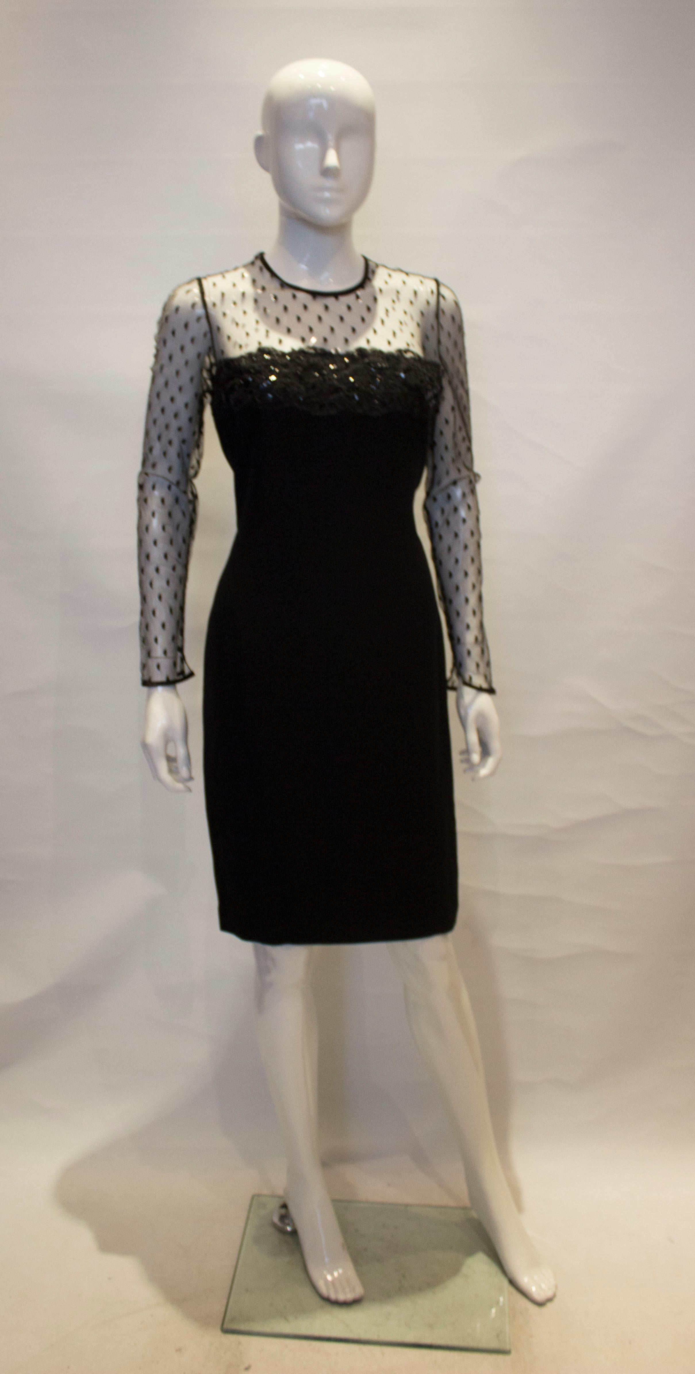 Une robe de cocktail noire chic d'Adrienne Vittadini. La robe a des manches en filet et une zone supérieure devant et derrière. Il est entièrement doublé, avec une fermeture éclair centrale au dos et une fente de 5 1/2'' au dos. 