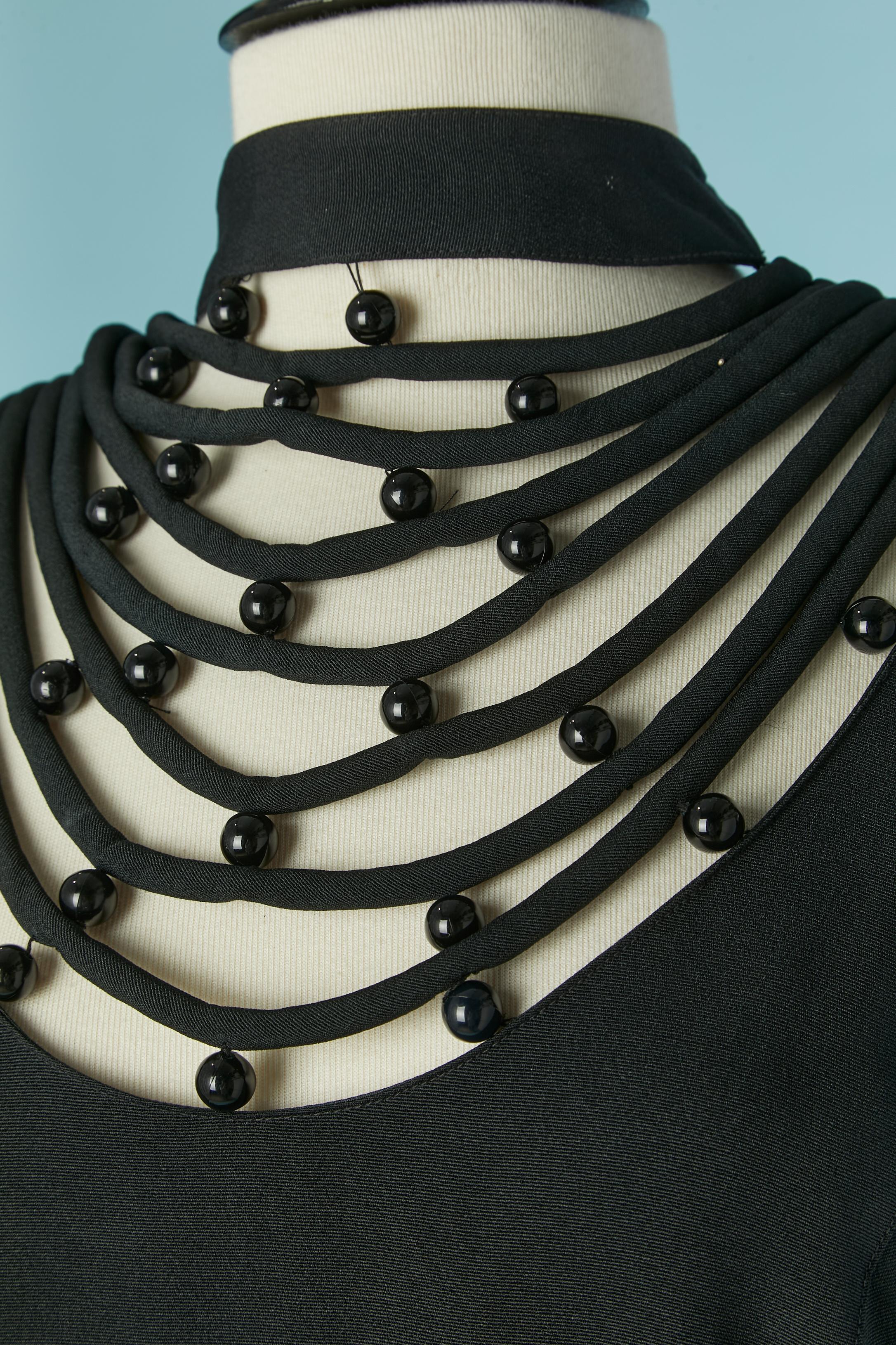 Robe de cocktail noire avec col transparent en perles et franges au dos avec bordures en perles. Composition du tissu principal et doublure : rayonne. 
Pad d'épaule. Bouton et boutonnière aux poignets. Fermeture à glissière au milieu du dos. Fente