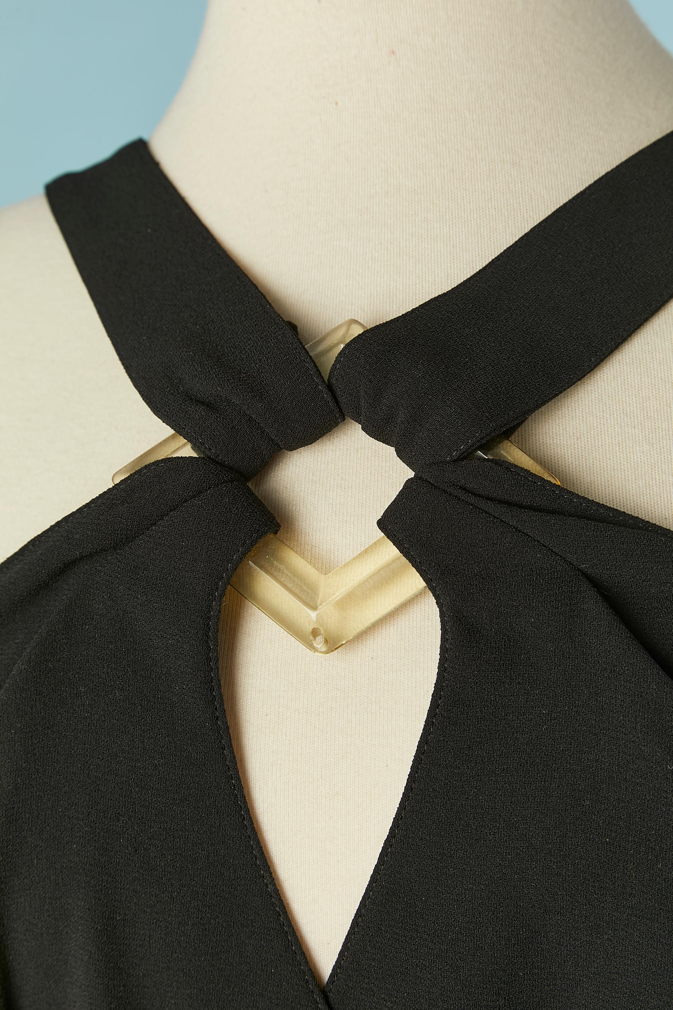 Abito da cocktail nero con fibbia in resina trasparente sul davanti e fascia sulla schiena. Cintura in Fabrice legata sul davanti. 
Tessuto principale: crêpe di poliestere. Fodera: poliestere. 
Chiusura a scatto al centro della schiena sulla vita.