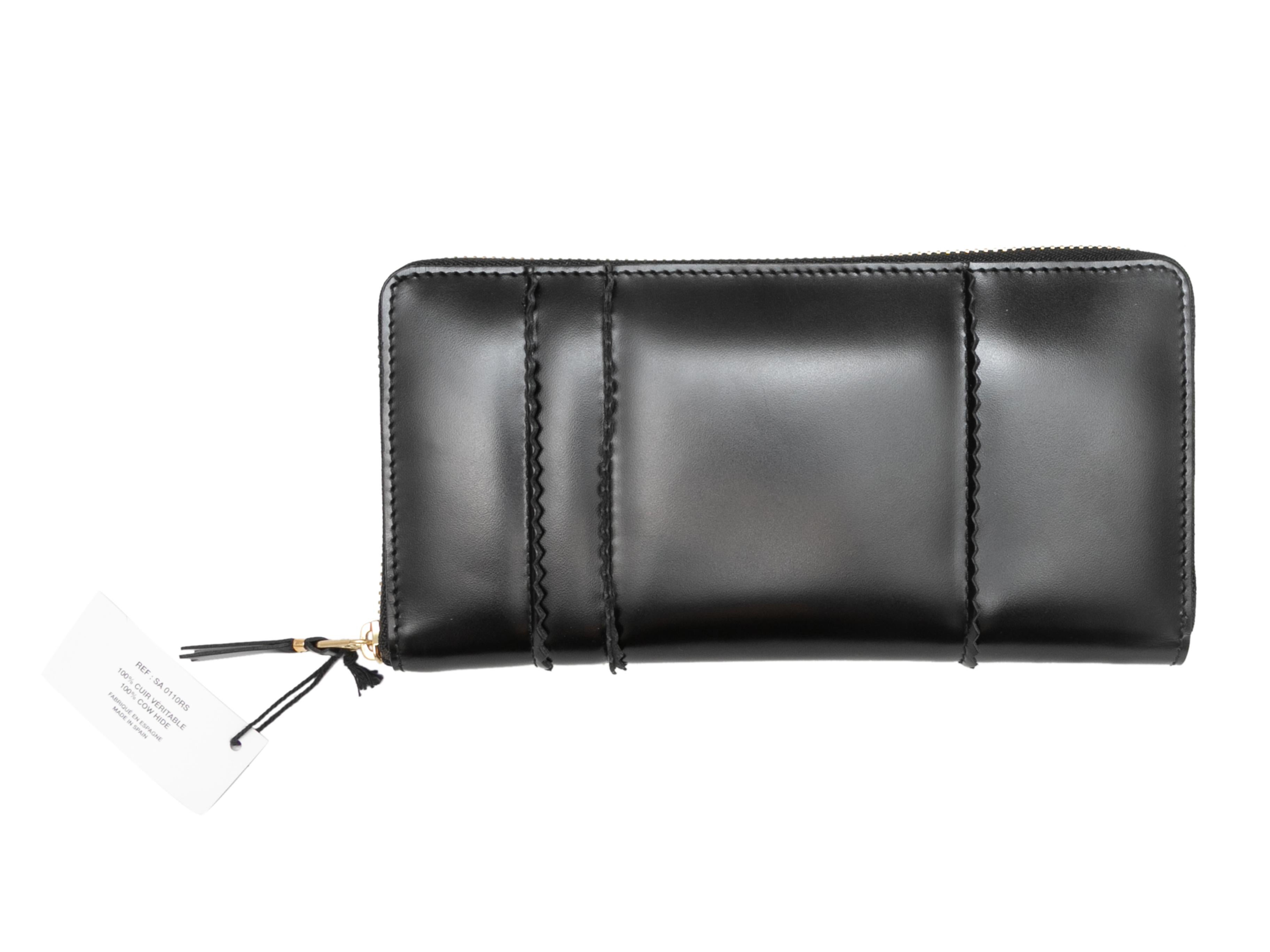 Black leather continental wallet by Comme Des Garcons. Gold-tone hardware. Multiple interior card and cash slots. Exterior zip closure. 8