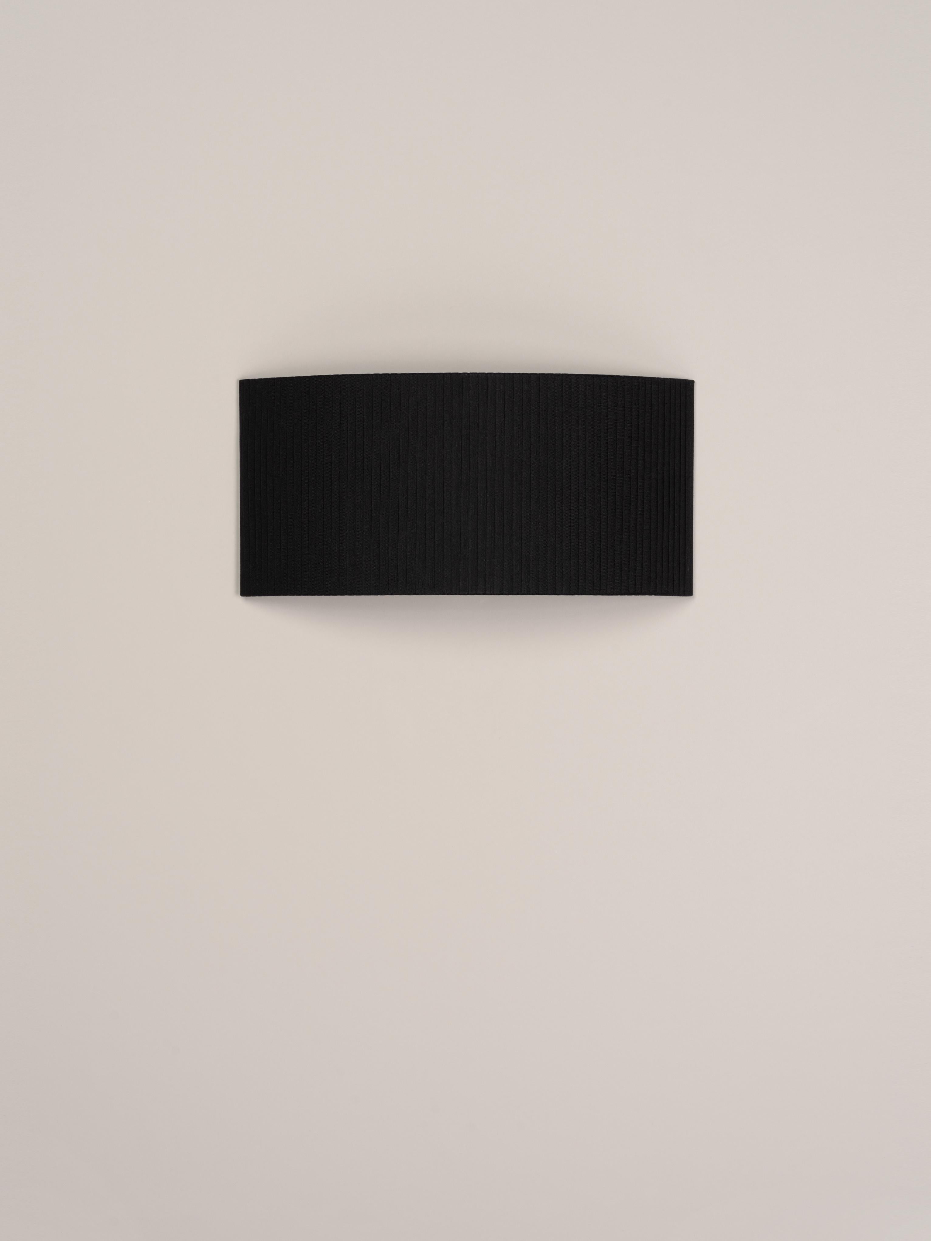 Black Comodín Rectangular wall lamp by Santa & Cole
Dimensions: D 50 x W 13 x H 24 cm
Materials: Metal, ribbon.

This minimalist wall lamp humanises neutral spaces with its colourful and functional sobriety. The shade is fondly hand-ribboned,