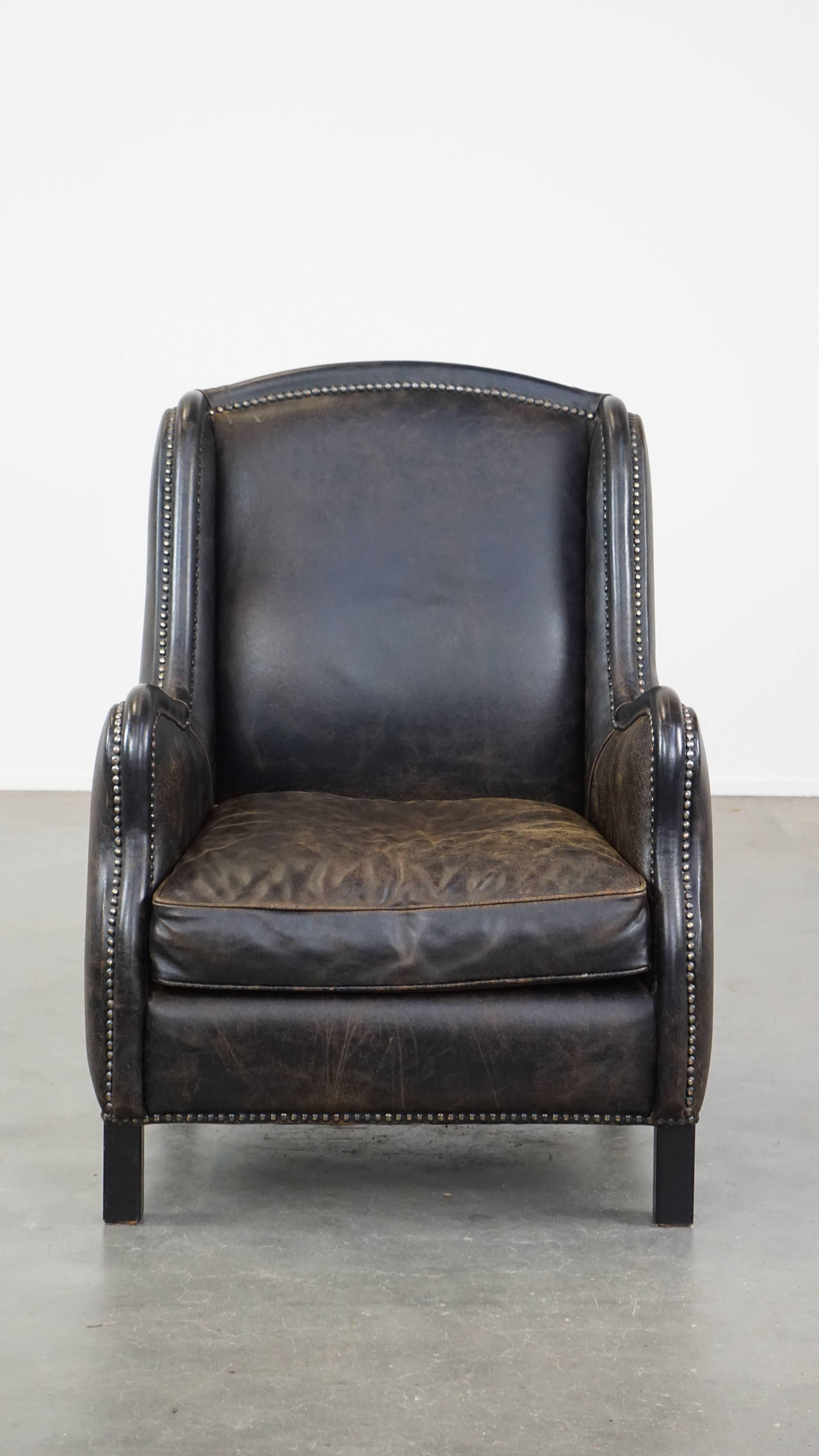 This fantastic black leather armchair easily fits into almost any interior. It features a high back and is finished with decorative nailheads. The armchair comes with a loose seat cushion and offers excellent seating comfort. Due to years of use, it