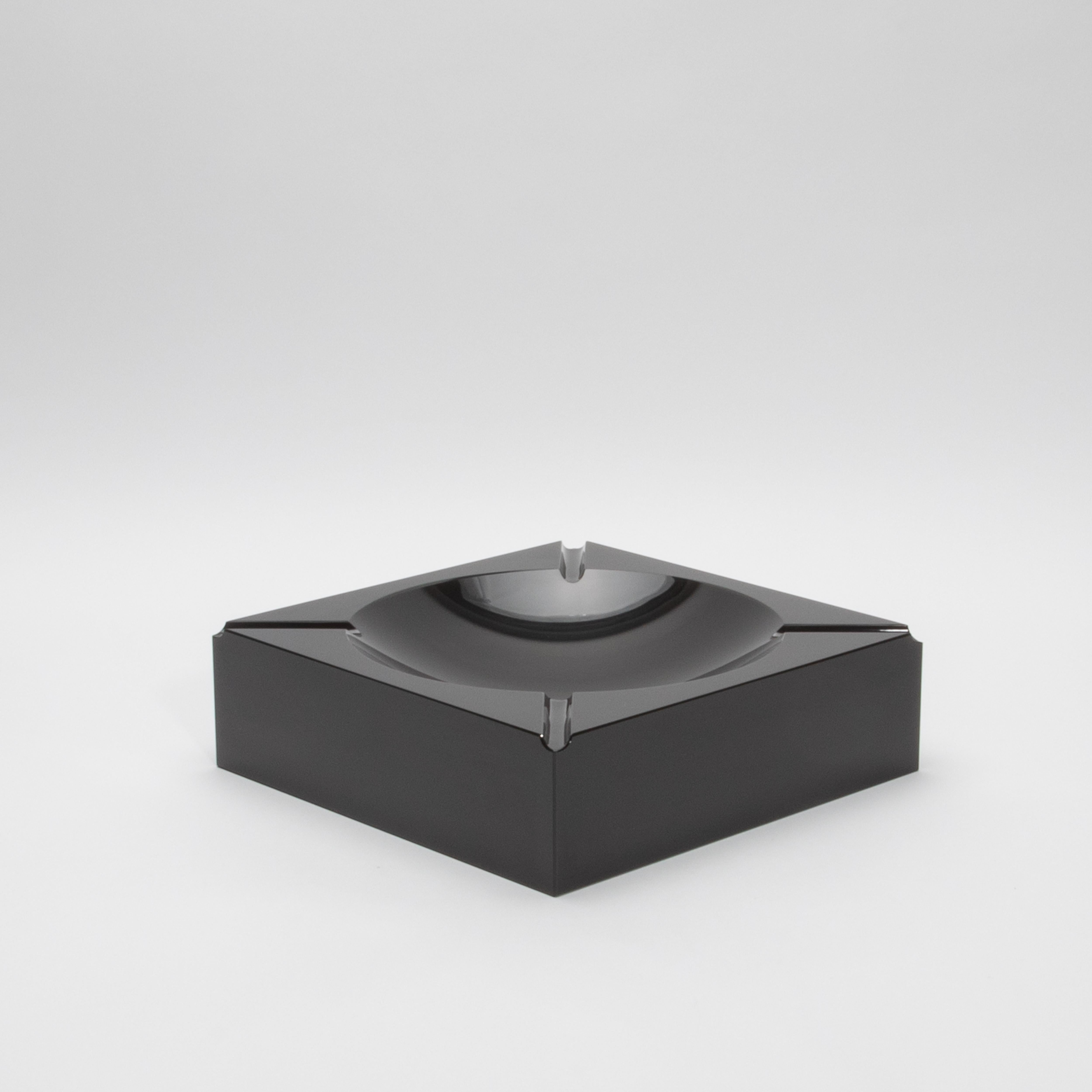 Este cenicero de cristal de KA Glass es una sorprendente pieza de artesanía, meticulosamente esculpida a mano en cristal de primera calidad. Su forma cuadrada minimalista emana una elegancia elegante y moderna, mientras que el tono negro intenso