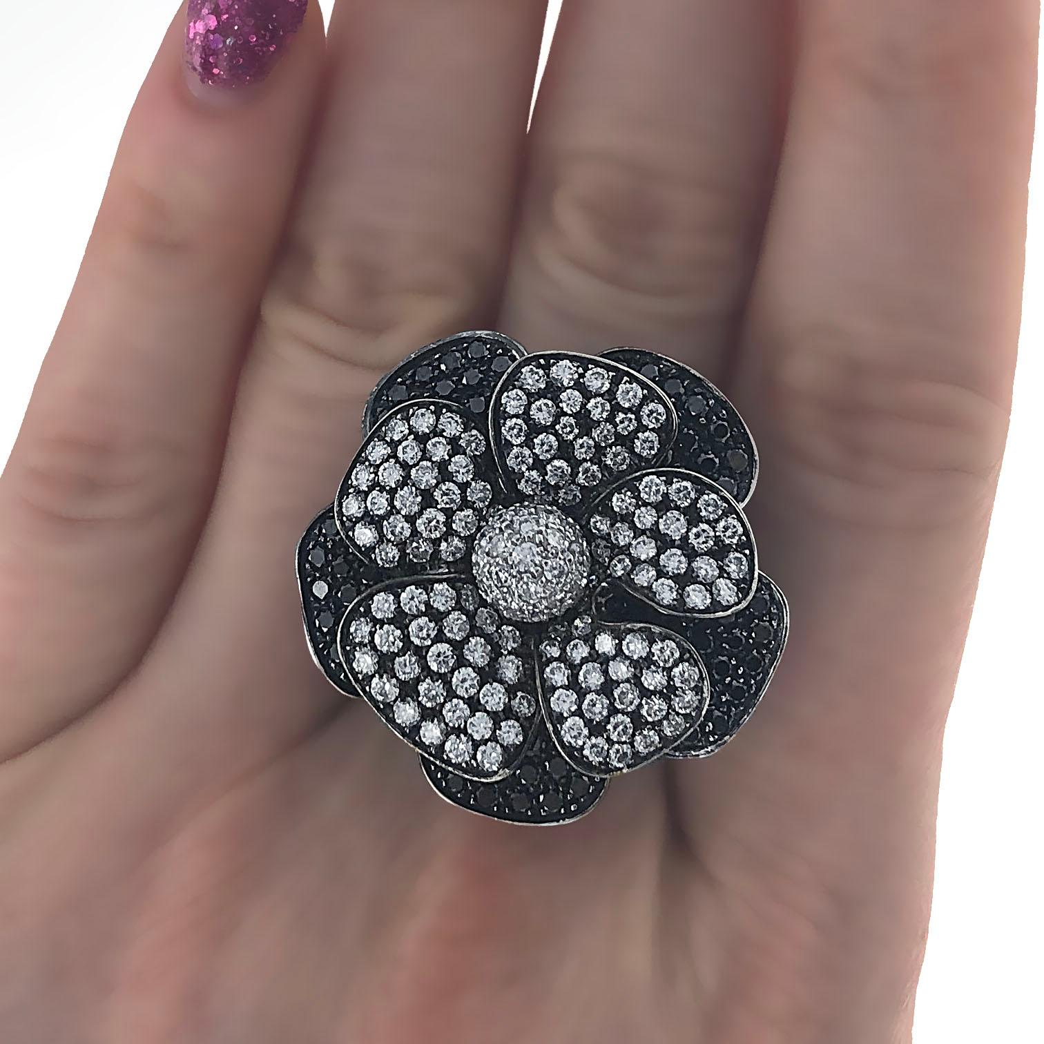 18 karat white gold black diamond and white diamond flower cocktail ring. The ring is made with white round brilliant diamonds and black round brilliant diamonds. The ring is made to look like flower petals.