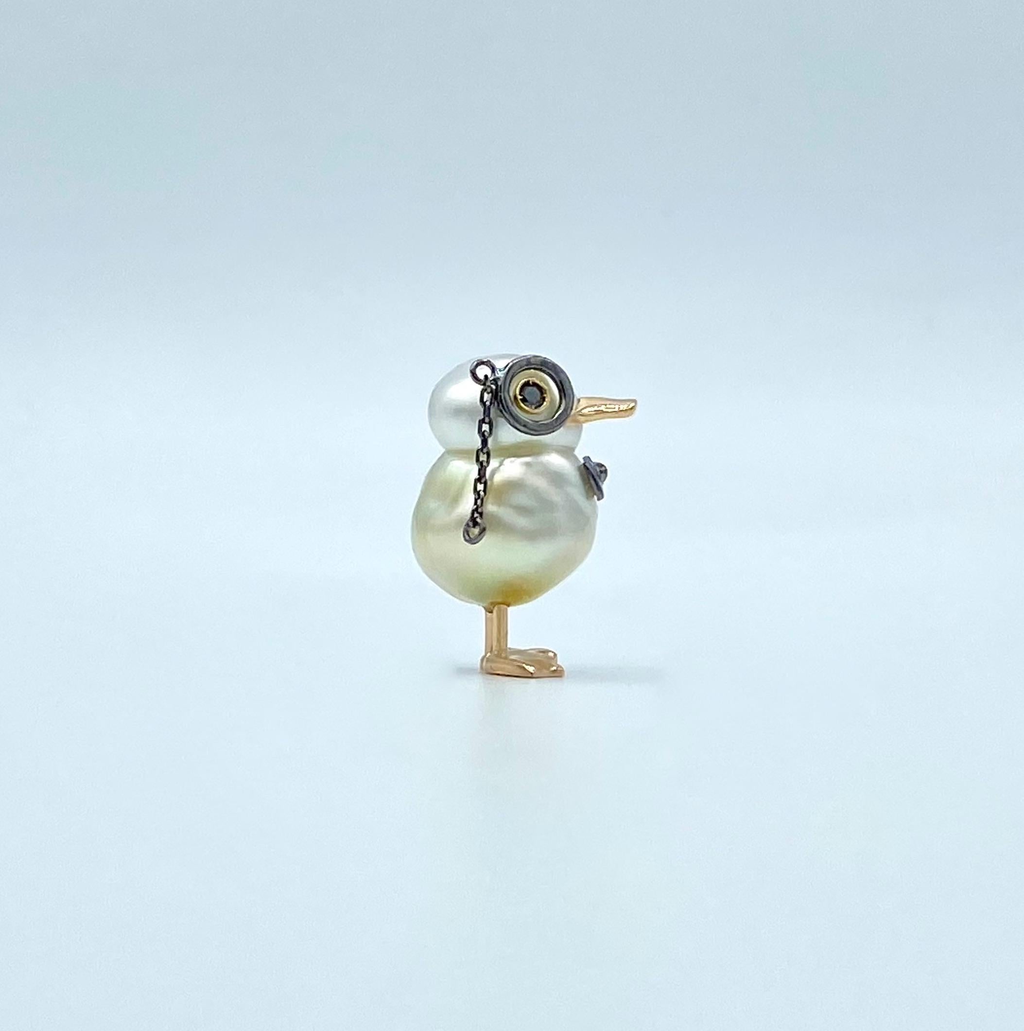 I used an Australian pearl measuring 11 x 15.5mm to make a cute duck that wears monocle and a bow tie  to wear as a jacket pin.
The 18KT gold used is red for the beak and legs. 
The 18Kt white gold monocle and bow tie are black rhodium