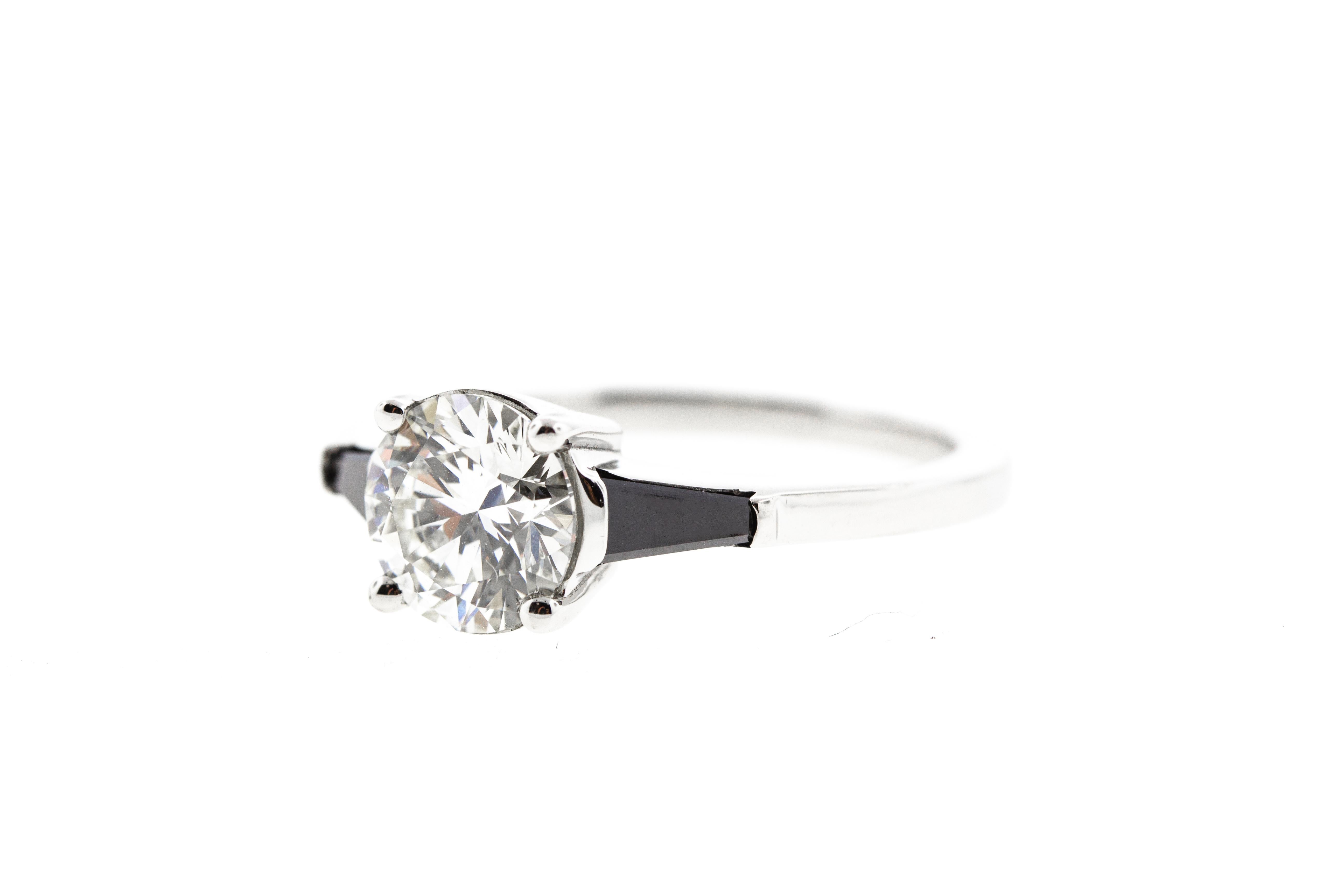 This ring is crafted in platinum, and contains a Round Diamond (1.08 total carat weight, G color, VS1 clarity) surrounded by 2 black diamond baguettes (0.24 total carat weight). With a raised profile and set in platinum, this ring is perfect for the