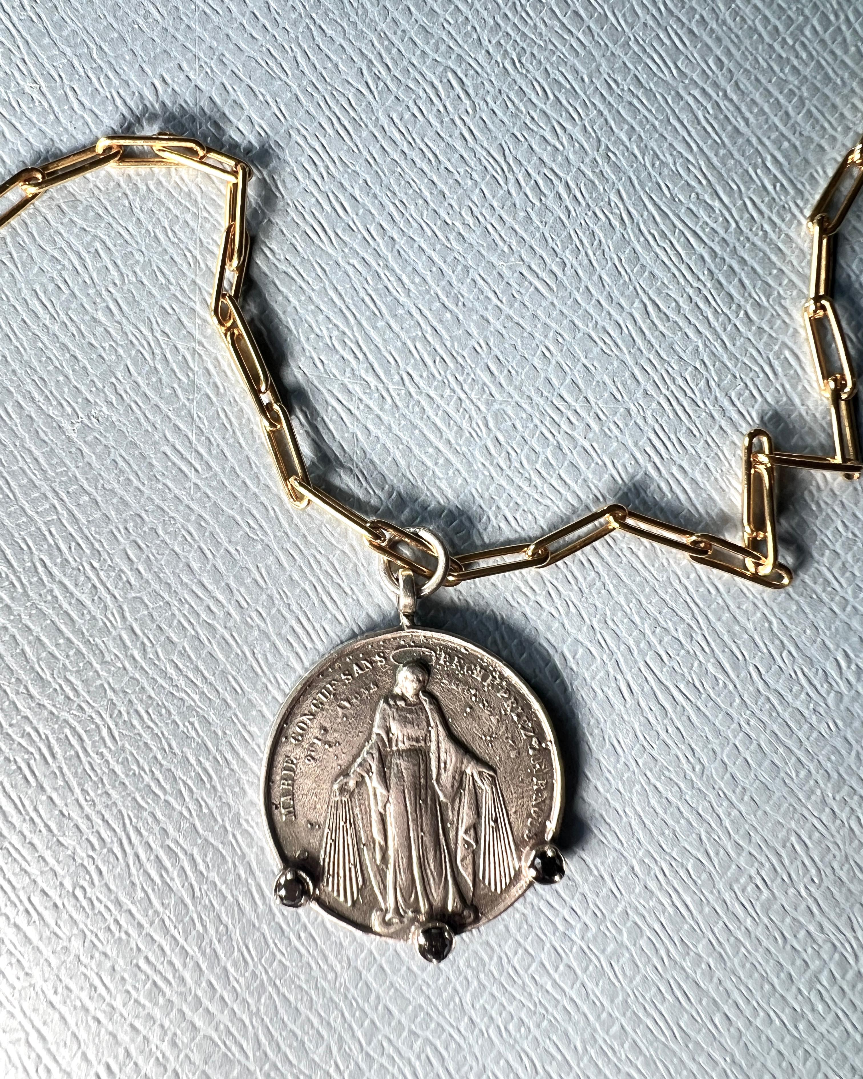 Ce collier médaille miraculeuse en argent fabriqué à la main représente la Vierge Marie sur une face et Saint Joseph tenant l'Enfant Jésus au revers. Suspendu à une chaîne en trombone plaquée or 14k, le pendentif associe une iconographie sacrée à un