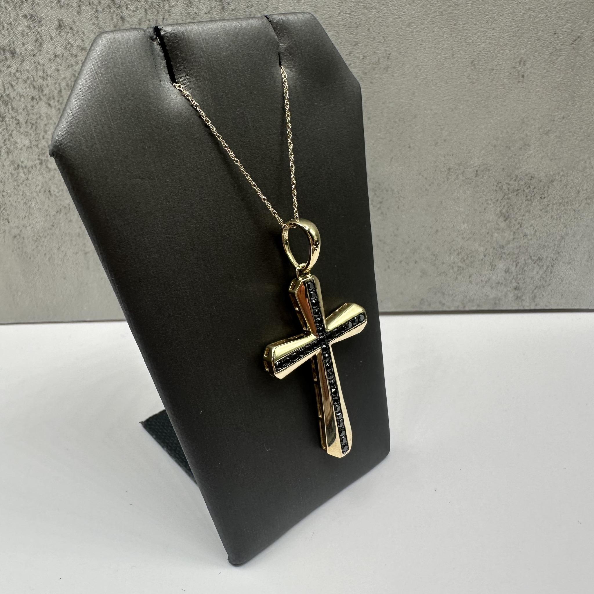 This striking Black Diamond Cross Necklace in 10kt yellow gold features 0.50ctw of round black diamonds, adding a bold and sophisticated touch to the cross design. The 18-inch length fits comfortably around the neck, and the spring ring clasp