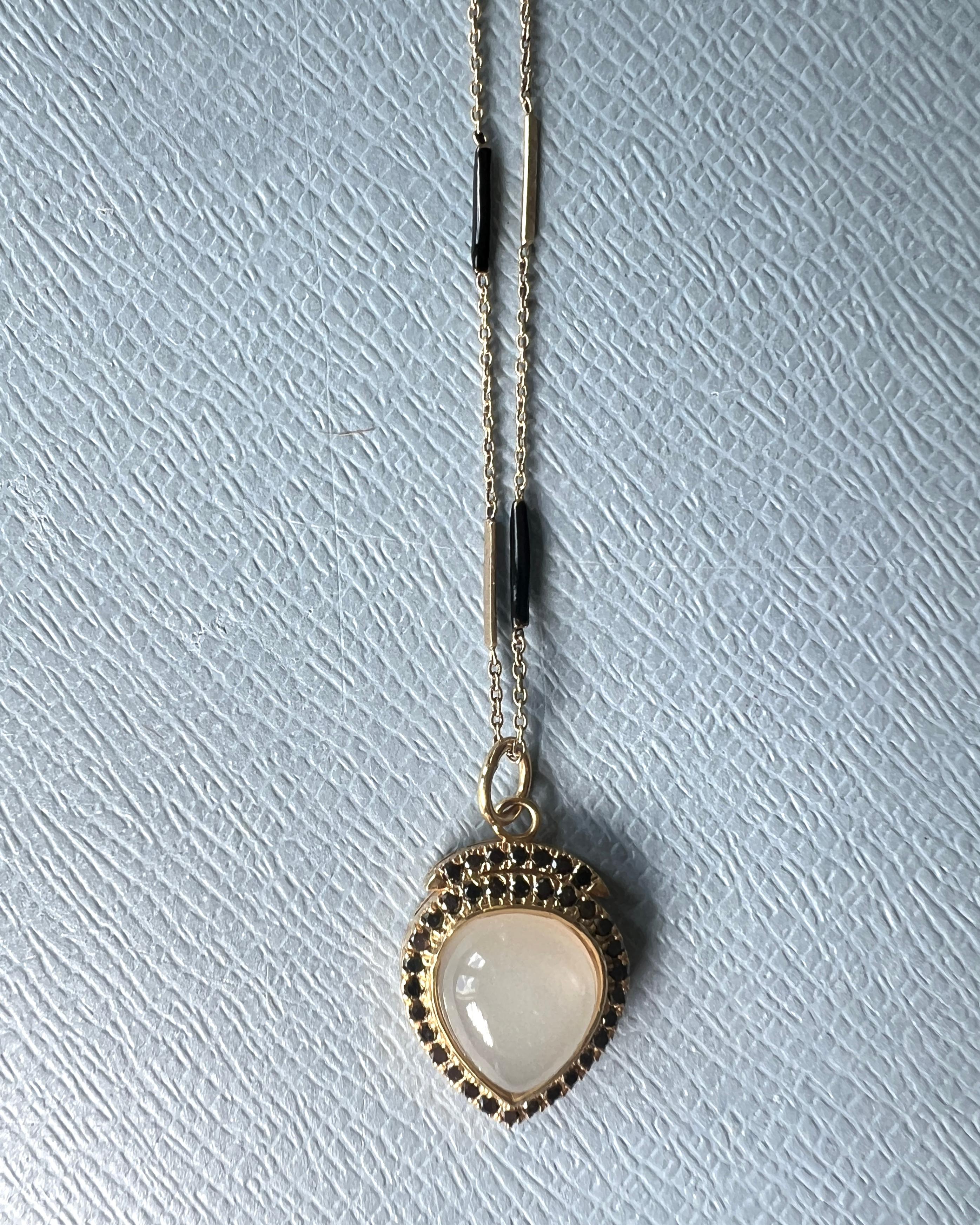 Diamante nero intorno a un cuore in pietra di luna Collana a catena in argento con smalto dipinto a mano

Catena: Argento placcato oro e dipinto a mano in nero.

Ciondolo a forma di cuore: Argento placcato in oro 14k

Gemme. Diamante nero e pietra