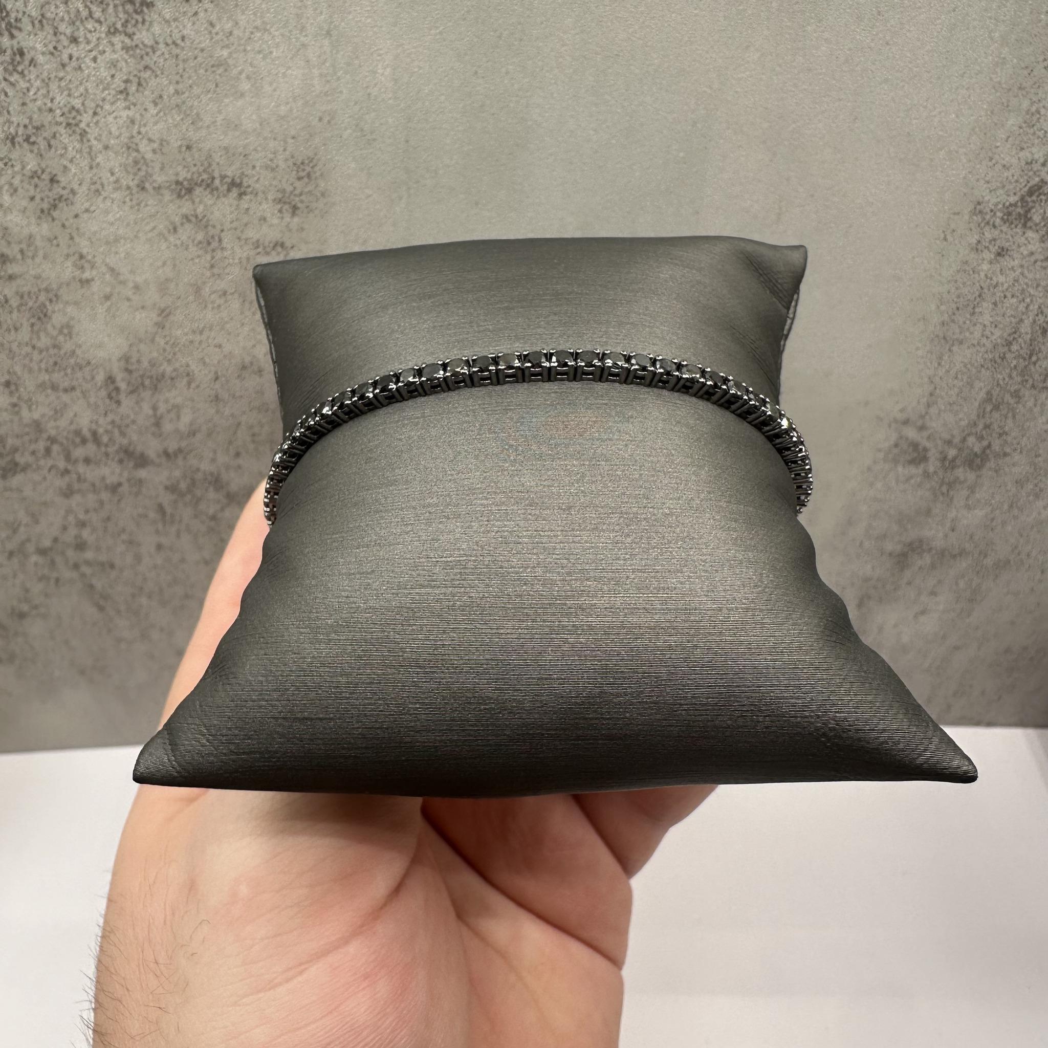 Esta llamativa pulsera de tenis de diamantes negros en oro blanco de 14 quilates presenta 4,84 quilates de peso total de diamantes negros redondos, cada uno engastado en rodiado negro para un aspecto atrevido y contemporáneo. Mide 20 cm de longitud