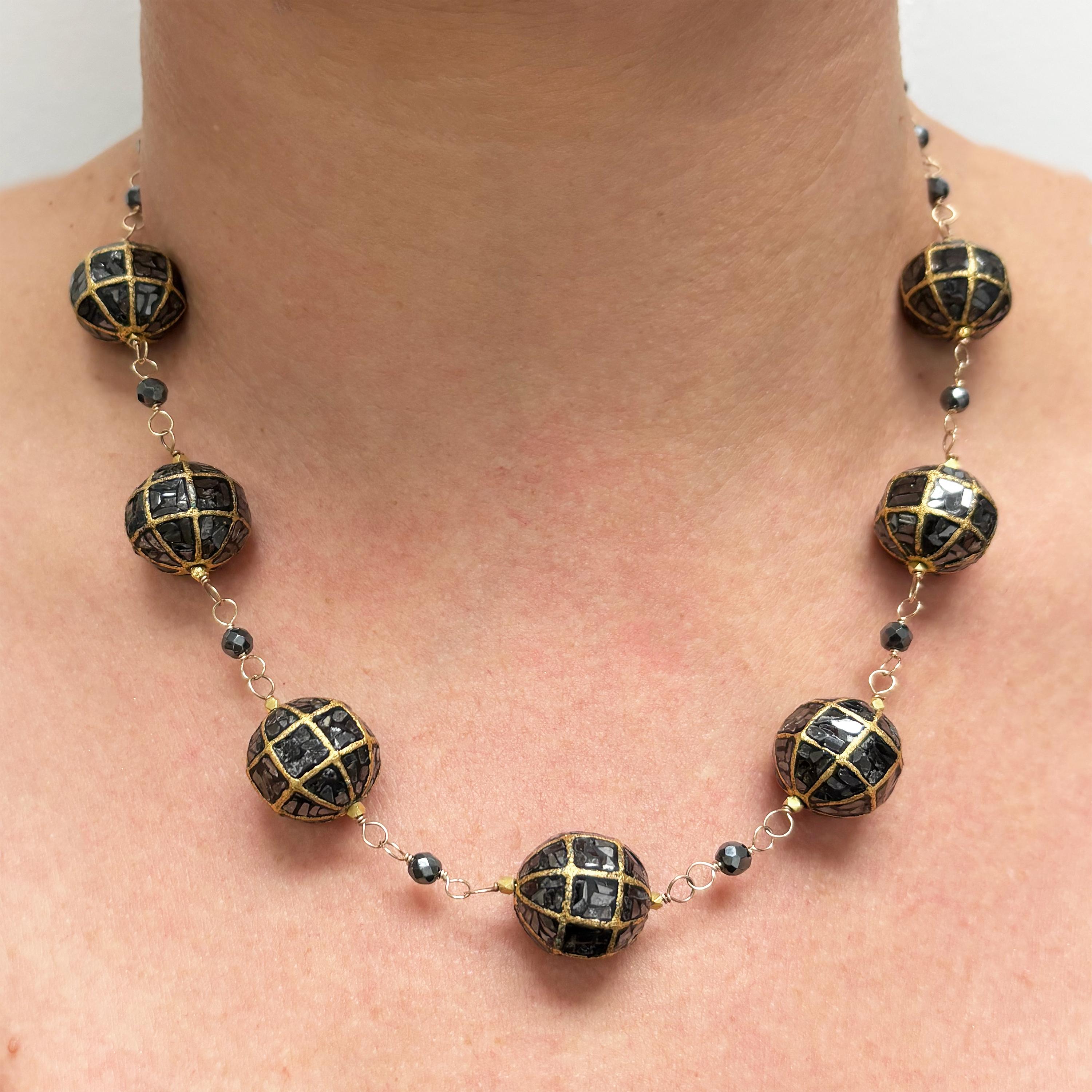 Description
Black diamonds encased within a bold 18k gold geometric-patterned sphere are flanked by radiant 20k faceted beads and accented with meticulously hand–wire-wrapped hematite. A striking composition that sets this piece apart and merges