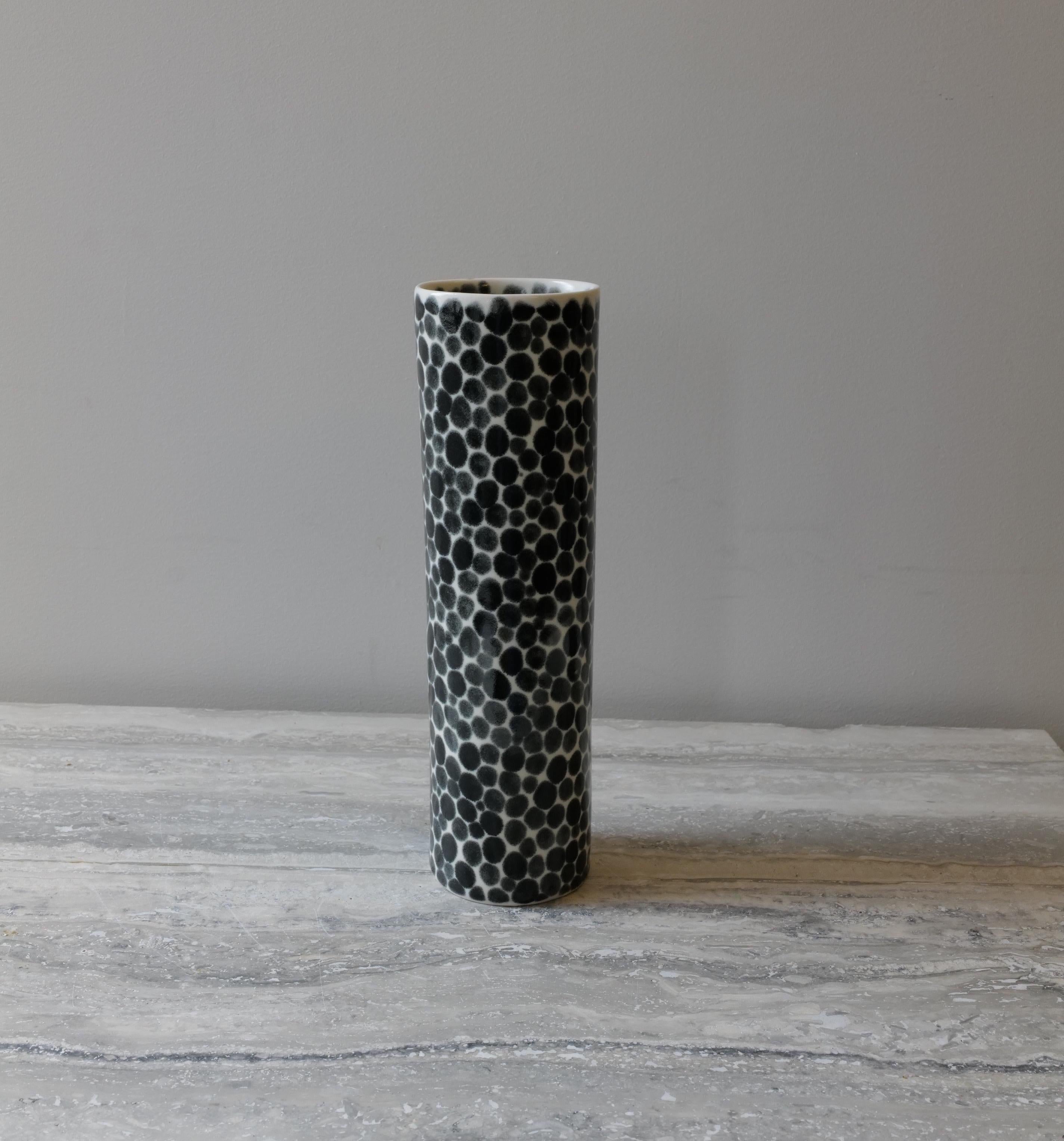 Tall, thin and elegant ceramic vase. Hand-cast in porcelain and once bisque fired, each dot is hand-painted with shiny black glaze. An unconventional layered glazing technique, developed by the artist, is used in these cast porcelain pieces. The