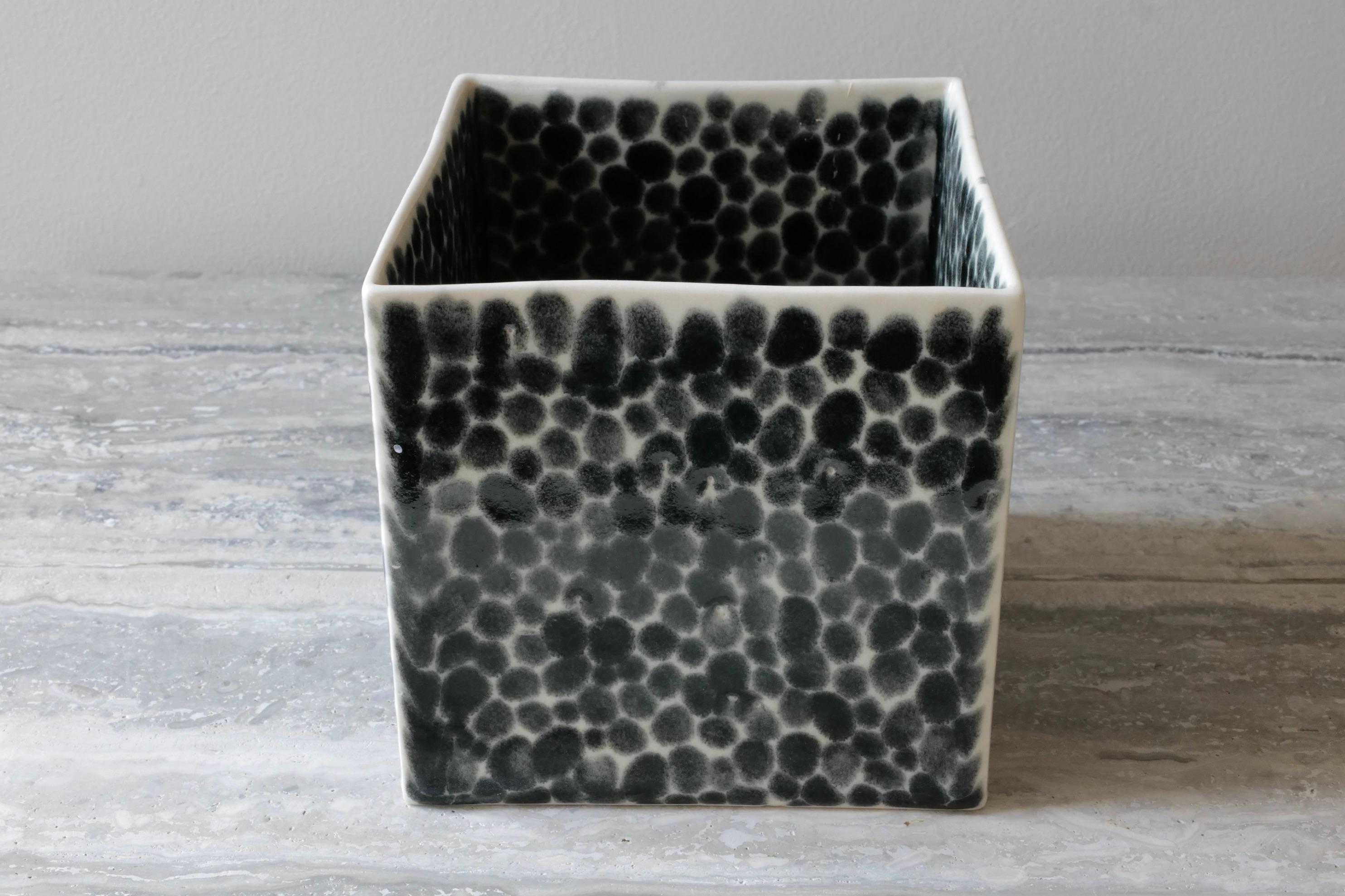 A large elegant open cube. Essentially multifunctional but displayed here as a vase. Hand-cast in porcelain and once bisque fired, each dot is hand-painted with shiny black glaze. An unconventional layered glazing technique, developed by the artist,