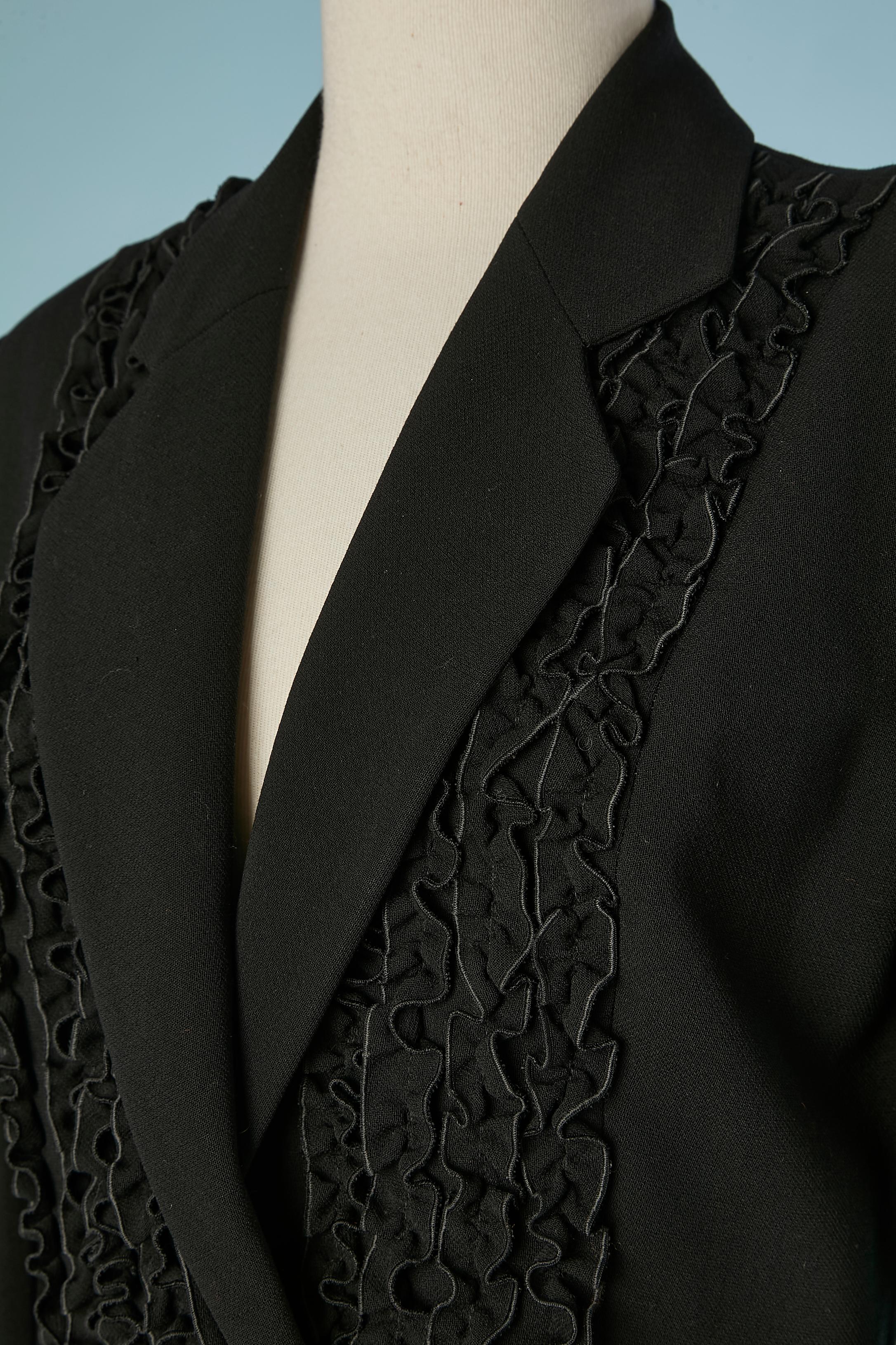 Veste noire à double boutonnage et à volants. Composition du tissu principal : 100% laine. Doublure : 60% acétate, 40% rayonne. 
Pochette sur les deux côtés. Fermeture par boutons et boutonnières sur le milieu du devant et sur les poignets. 
TAILLE