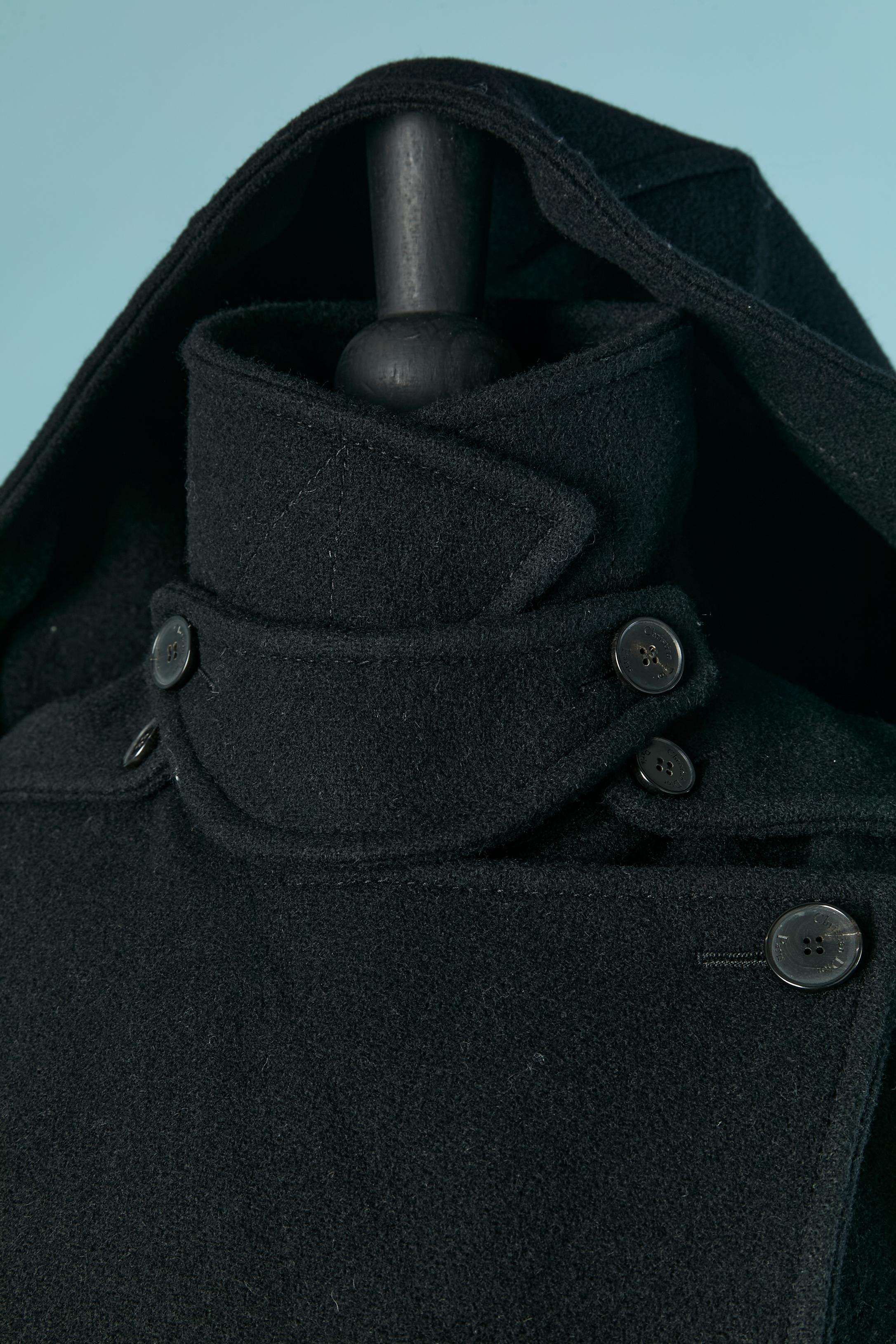 Black double breasted wool coat with nylon padded vest underneath and hood. Button inside to attach and detach the vest. Branded button and buttonhole on the front and on the half-belt on the back. Box pleat on the middle back. Detachable hood. 4