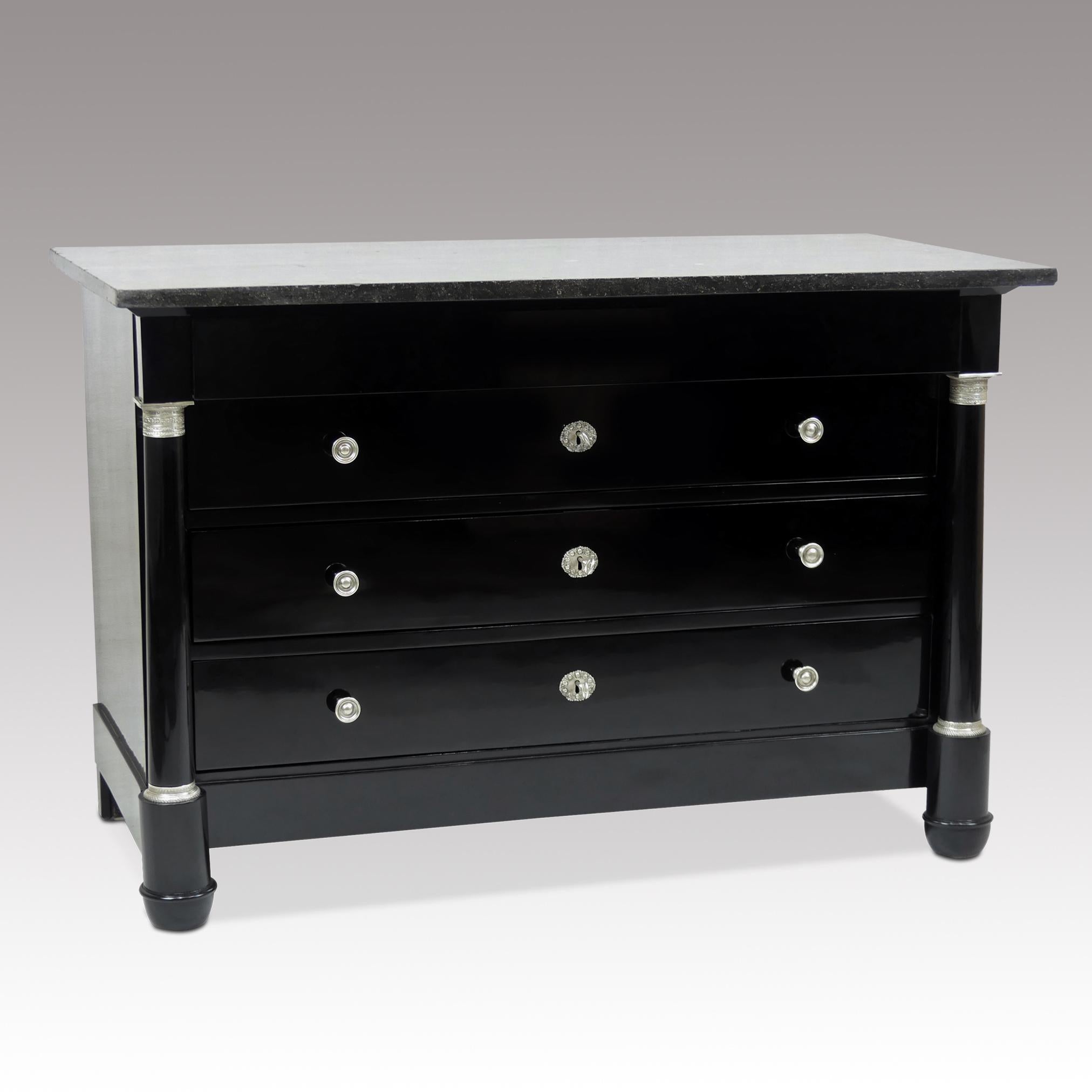 Antique ebonized Empire chest of drawers with silver-plated bronze fittings and original black / gray marble top. The dresser has four drawers and two columns, one on each side. The columns above and below are decorated with very fine, chased,