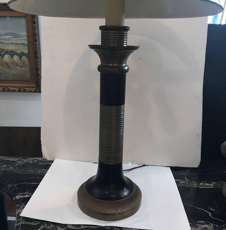 A brass and black enamel table lamp by Chapman. The brass shade is supported by a ribbed brass column with black enamelling. The lamp takes two standard bulbs.
Original finish has slight aging and some flecks to white lined brass shade.