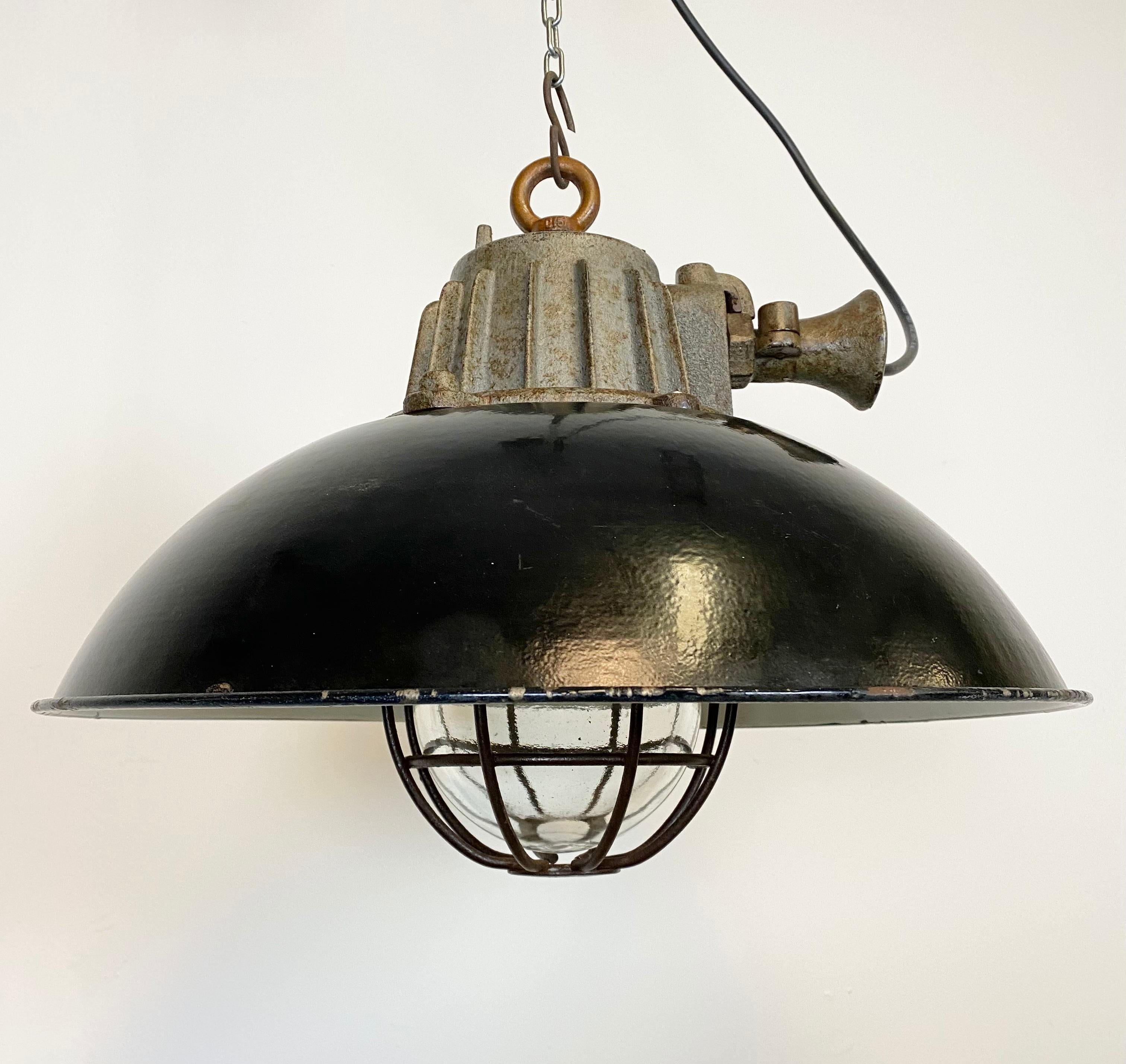 Industrial hanging lamp manufactured during the 1950s in former Czechoslovakia. It features a black enamel shade, white enamel interior, cast iron top, clear glass cover and iron grid. Porcelain socket for E 27 lightbulbs and new wire. The weight of